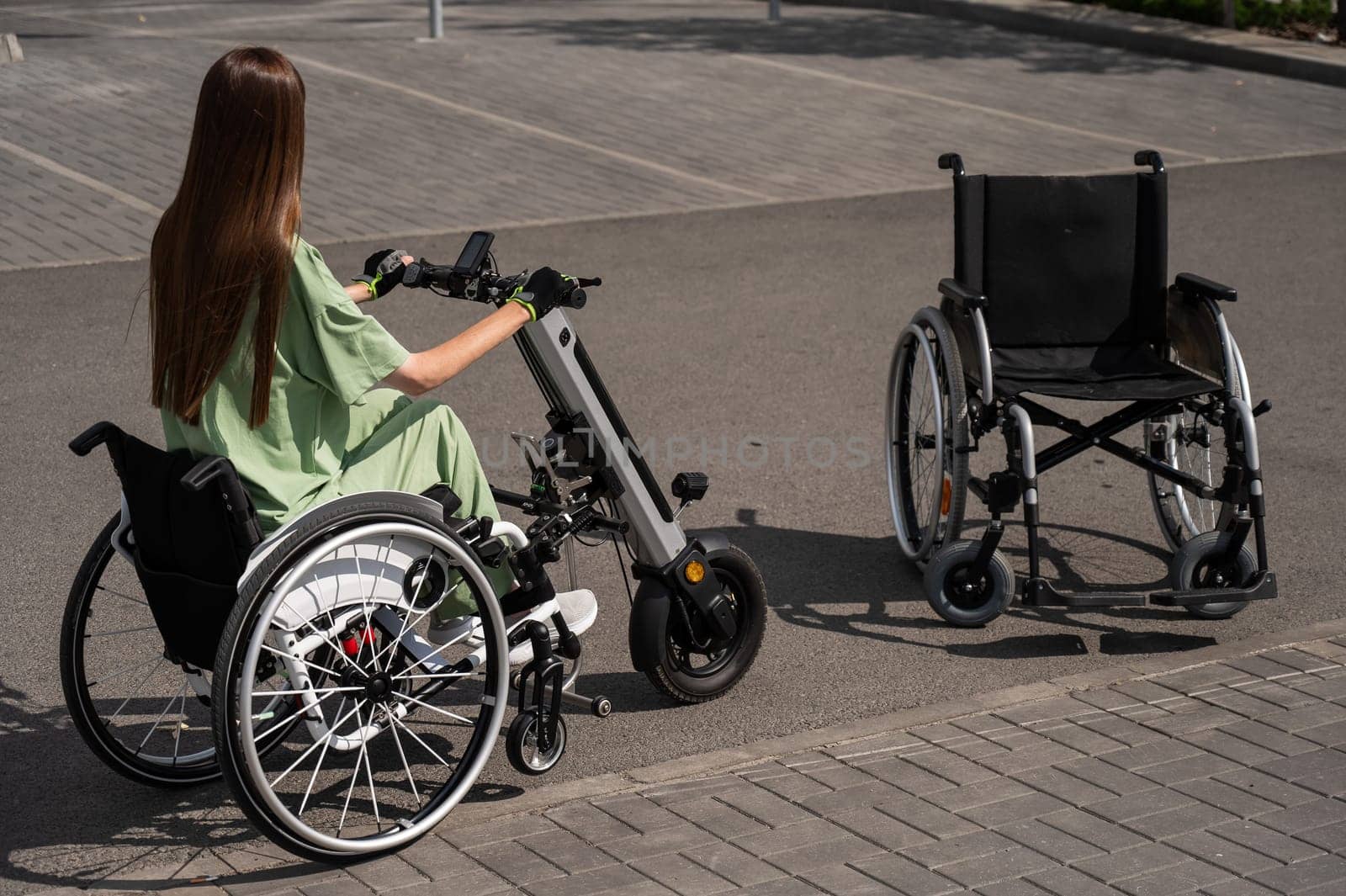 Woman in wheelchair with assistive device for manual control next to classic wheelchair. Electric handbike. by mrwed54