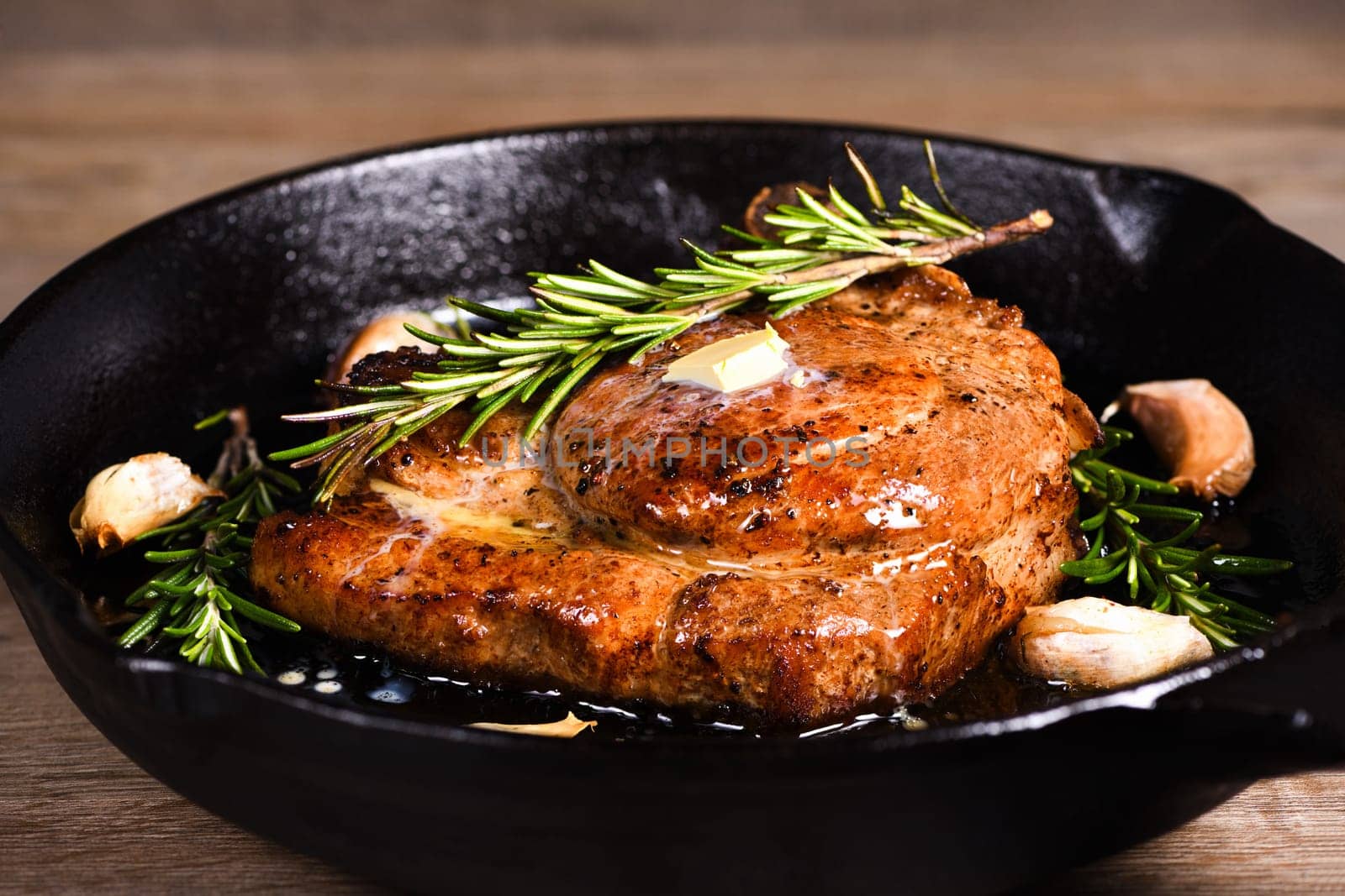 Pork cutlet on the bone in a piece of butter with garlic and rosemary in a frying pan 