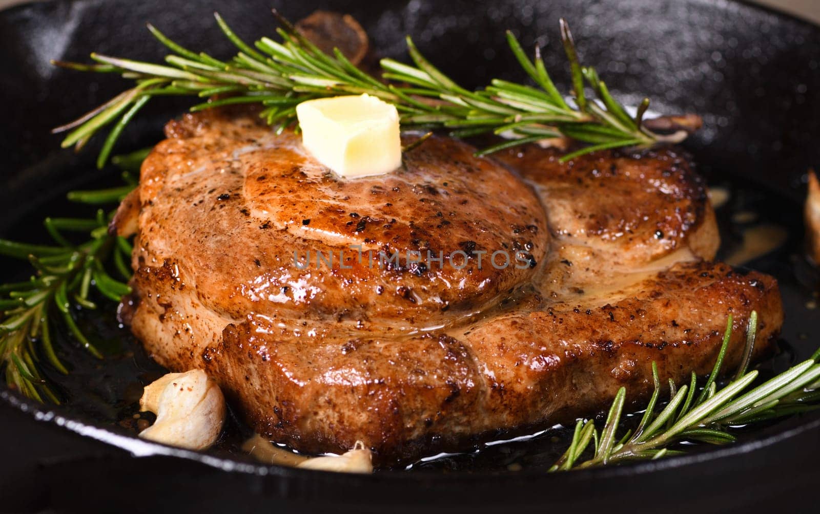 Pork cutlet on the bone in a piece of butter with garlic and rosemary in a frying pan 