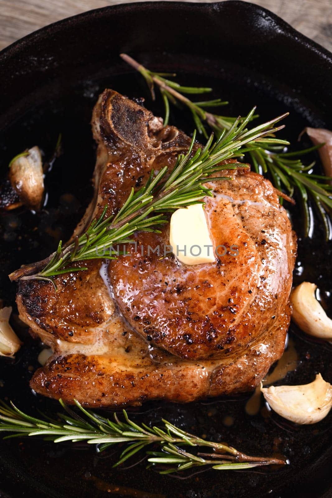 Pork cutlet on the bone in a piece of butter with garlic and rosemary in a frying pan 