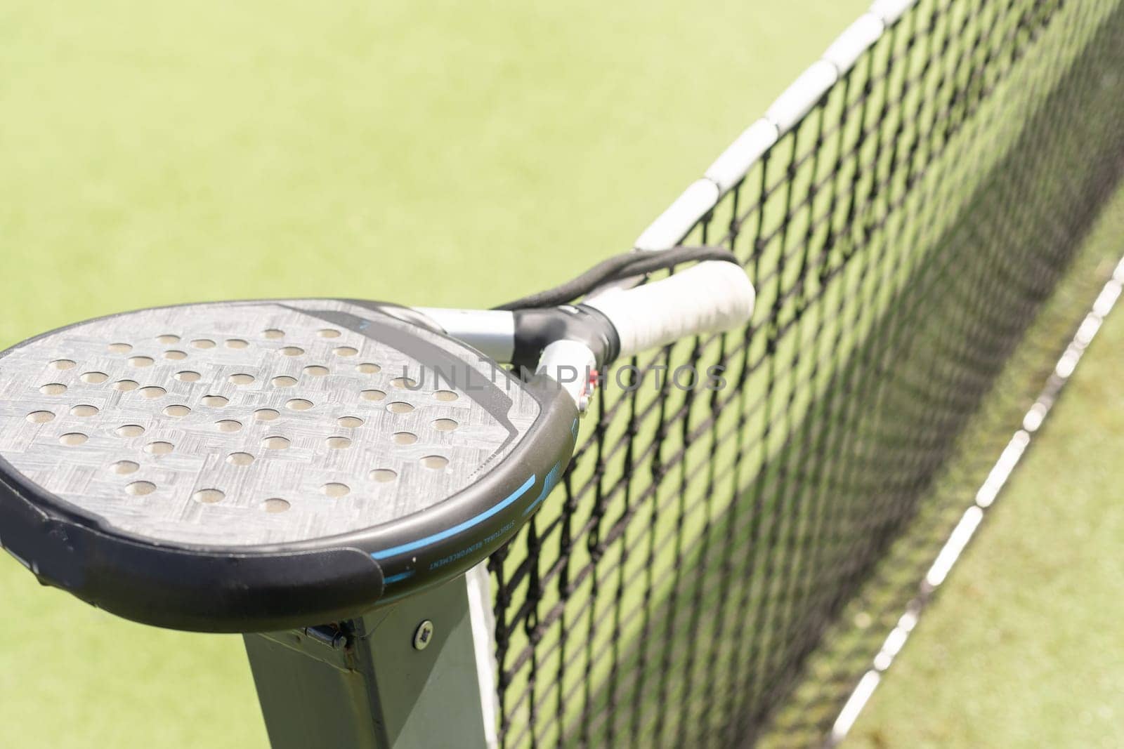 Padel racket and padel ball on a green court in the sunset. High quality photo