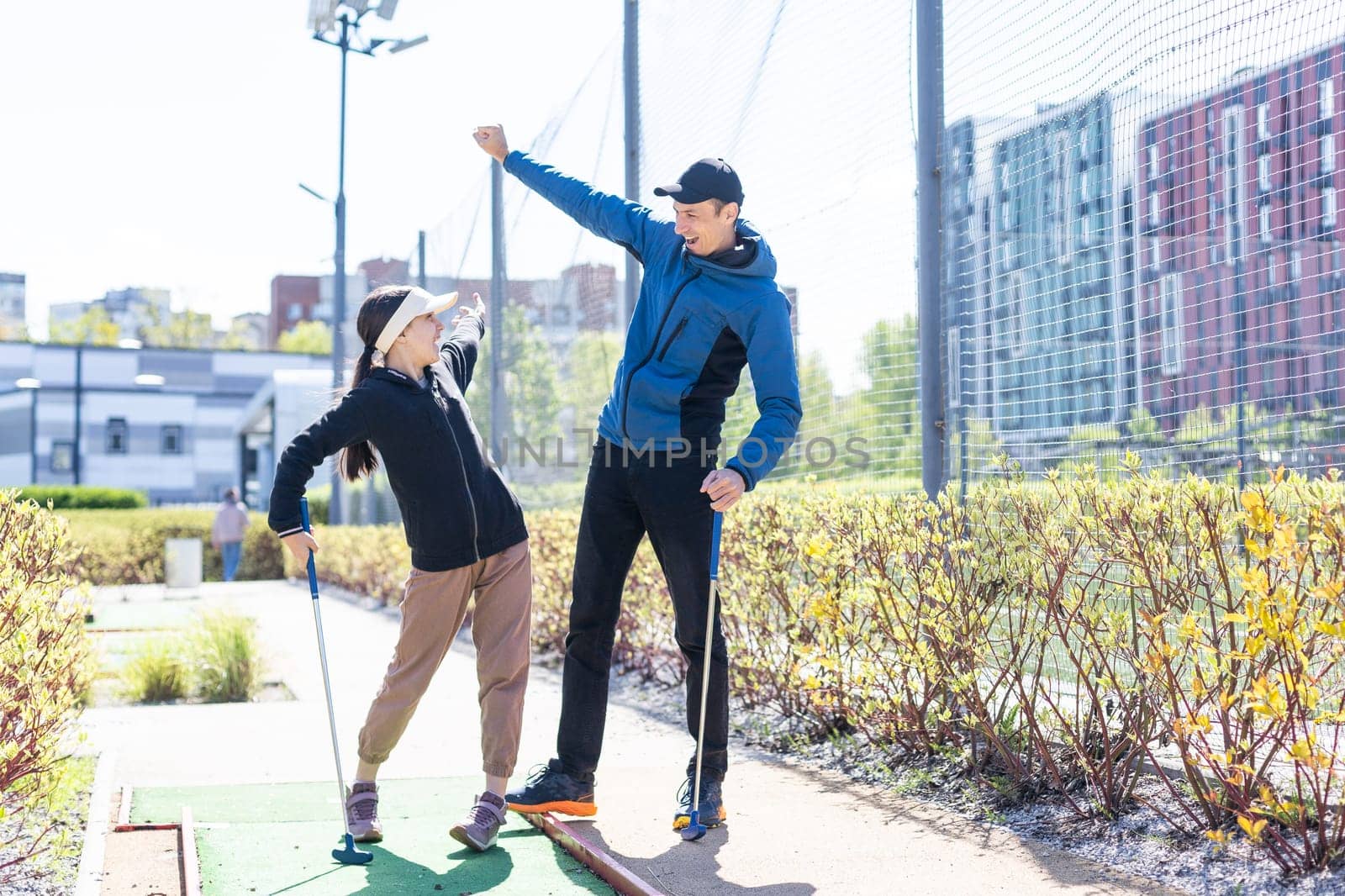 Sharing with golf experience. Cheerful young man teaching his daughter to play mini golf at the day time. Concept of friendly family. High quality photo