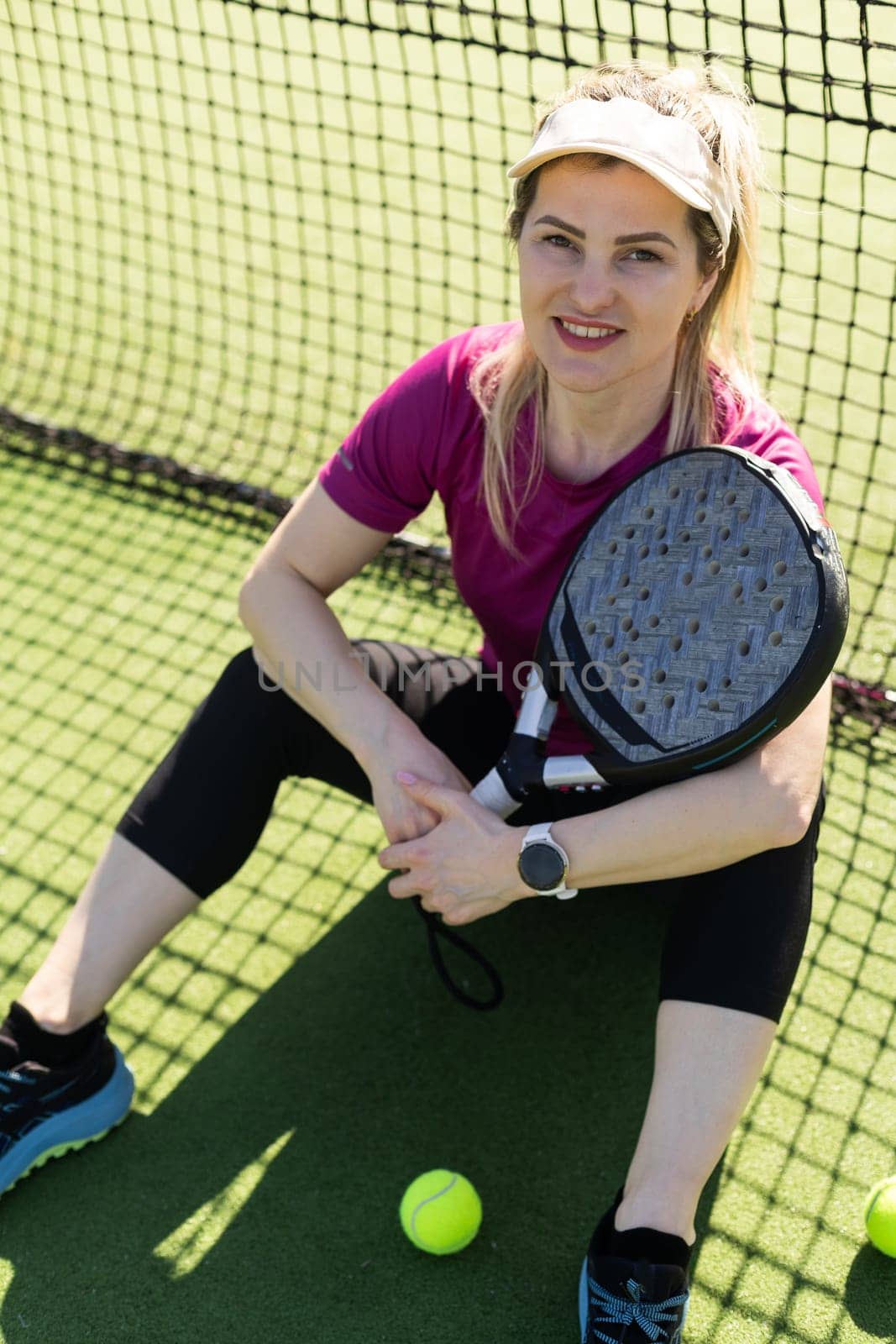 Young female smiling and looking at camera while playing padel against green background. High quality photo