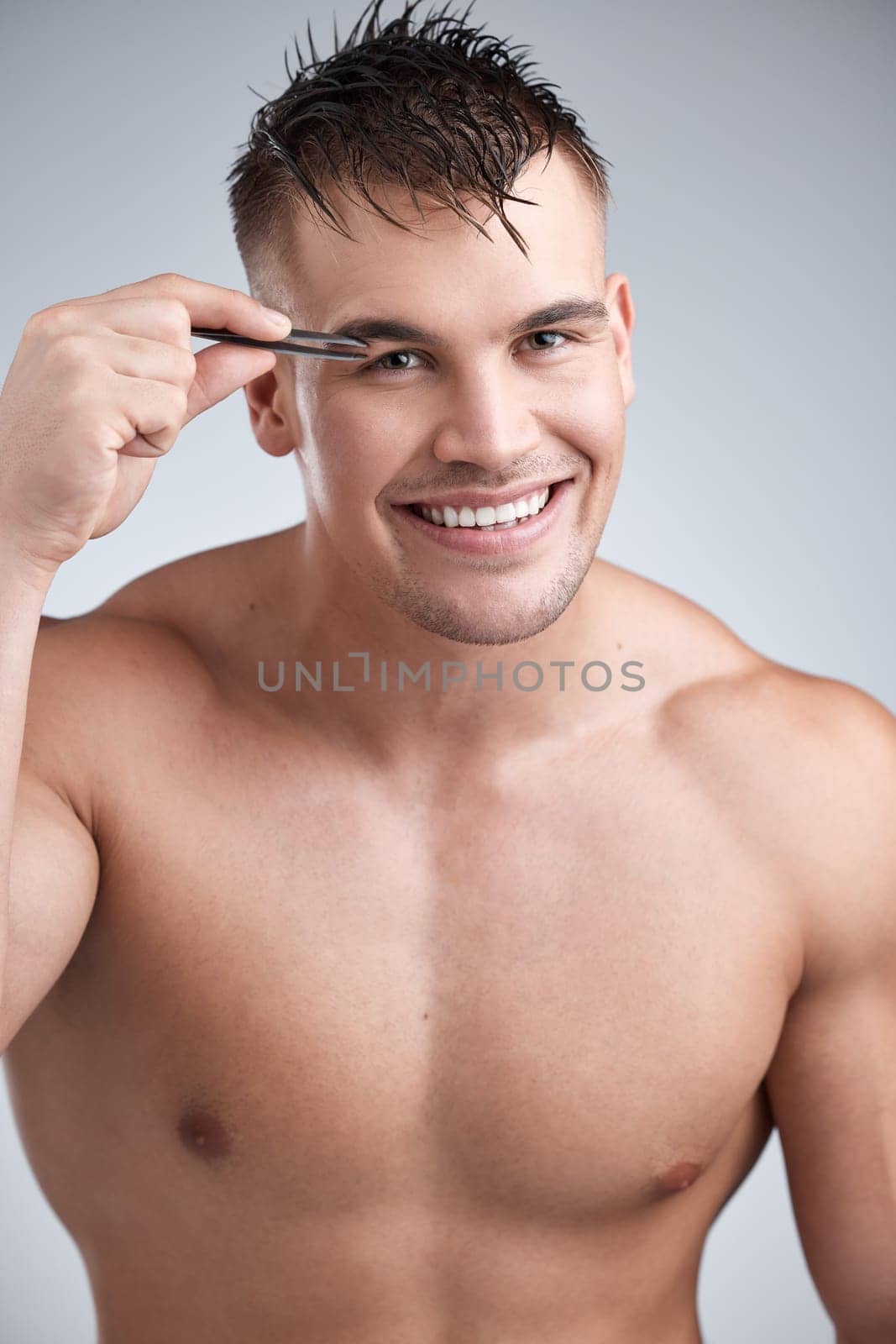 Man, portrait and grooming eyebrow hair with tweezer in studio background with body, smile and skincare with hygiene. Wellness, cleanliness and beauty with hands and routine with confidence for face by YuriArcurs