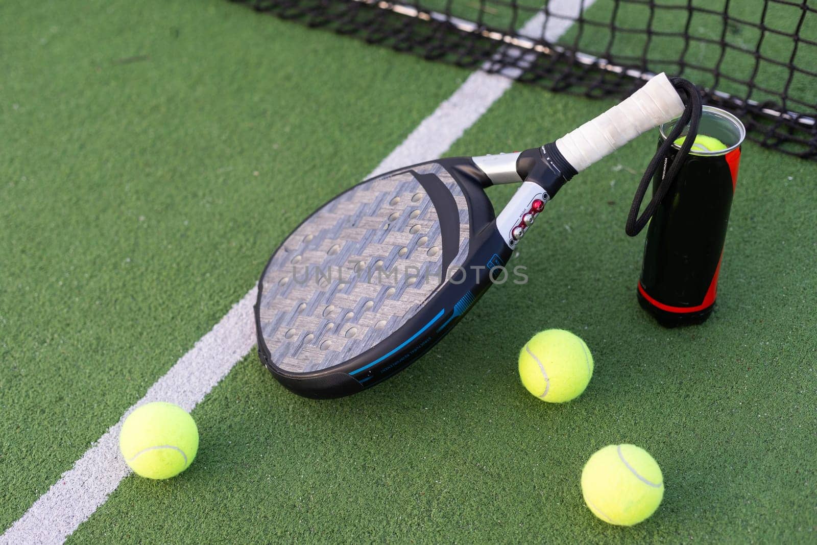 Blue padel racket and yellow balls placed on court near net on sunny day. High quality photo