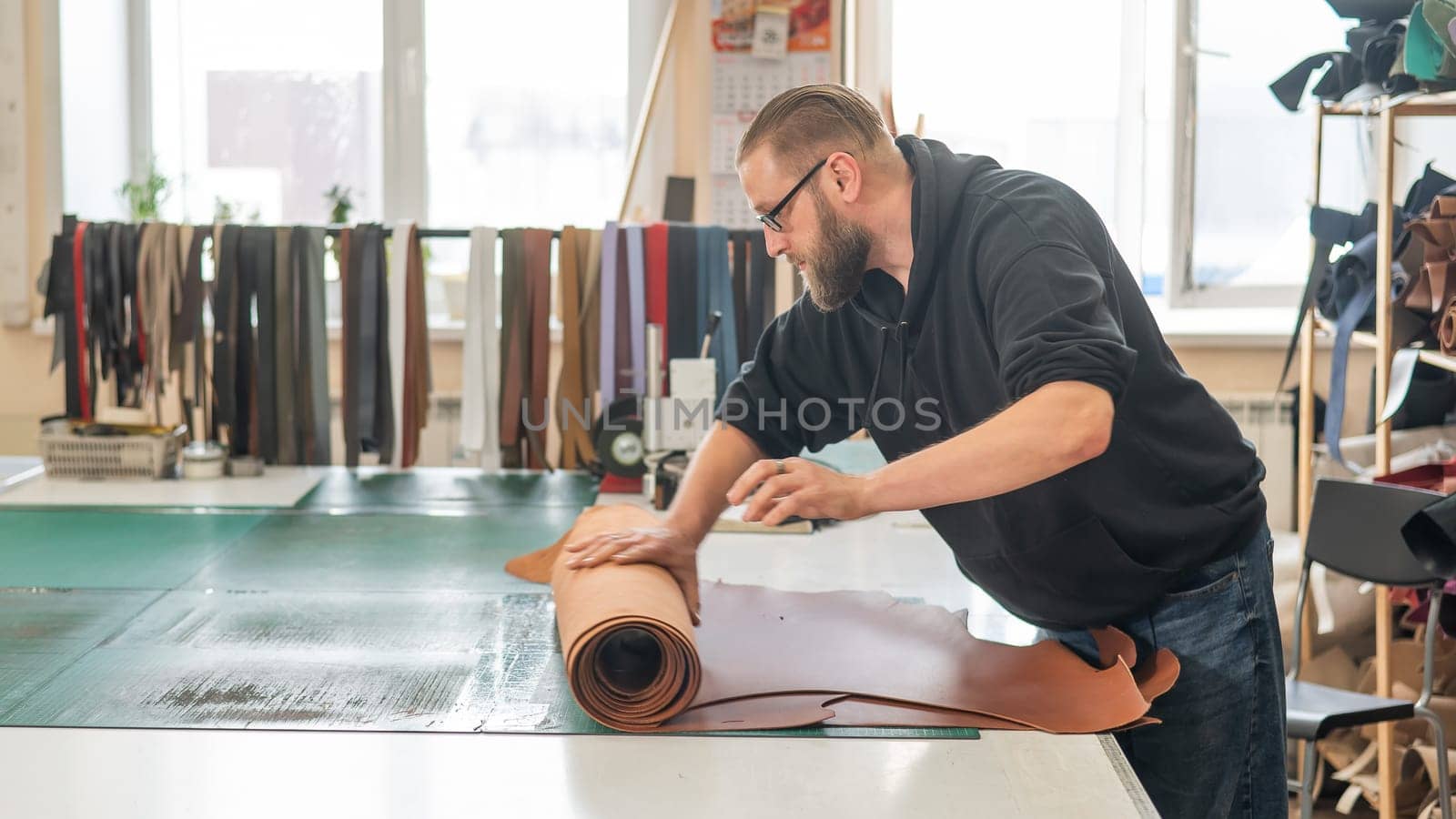 Leatherworker unrolls rolls of leather in workshop. by mrwed54
