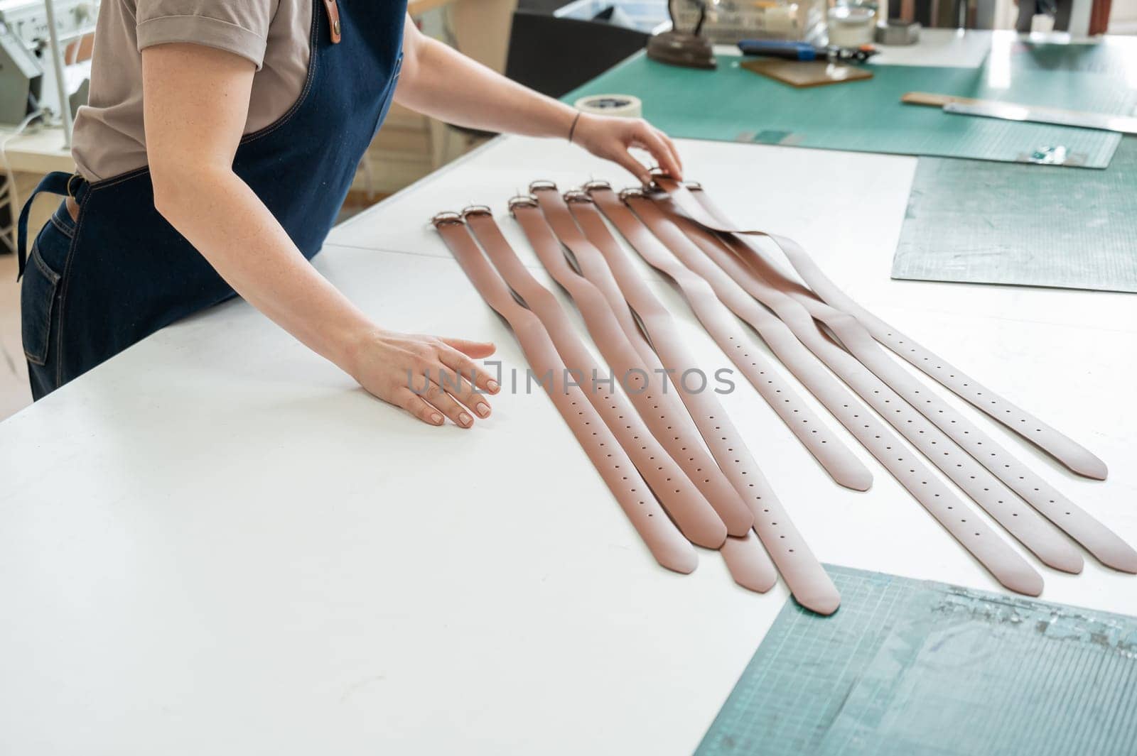 Close-up of a Caucasian woman's hands making genuine leather belts in a workshop. by mrwed54