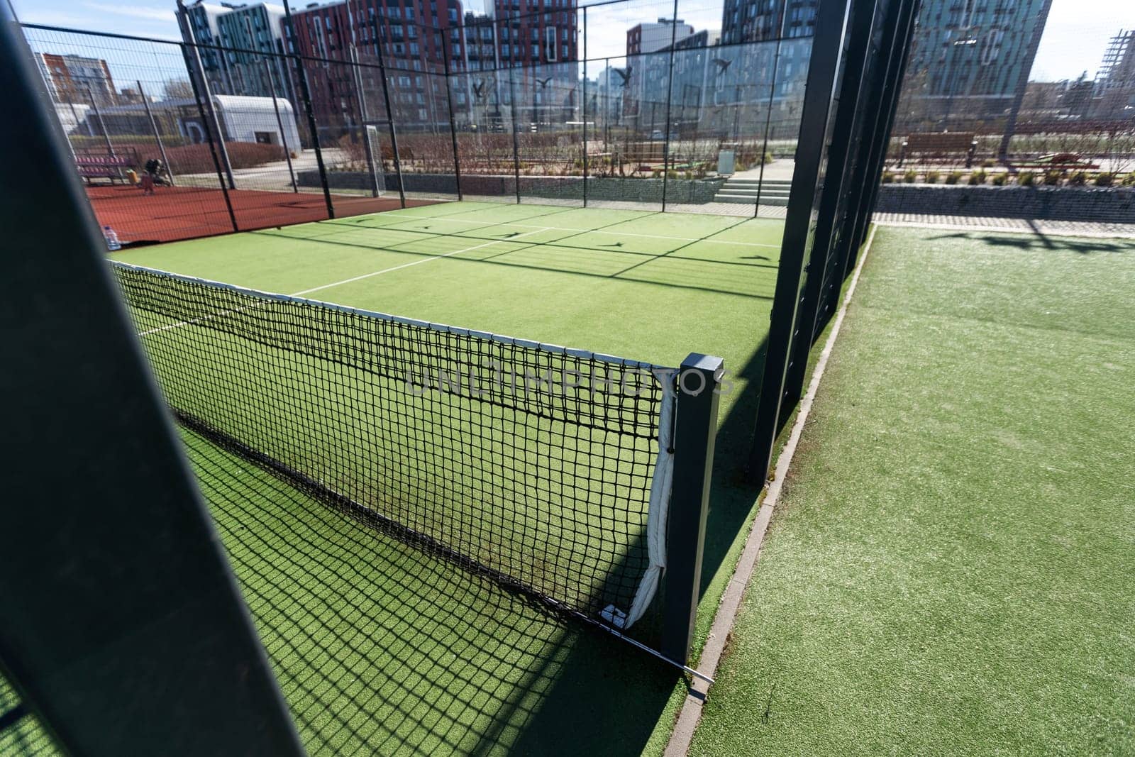 Landscaped areas of a residential development with a tennis court with high Plexiglas and metal fences. High quality photo