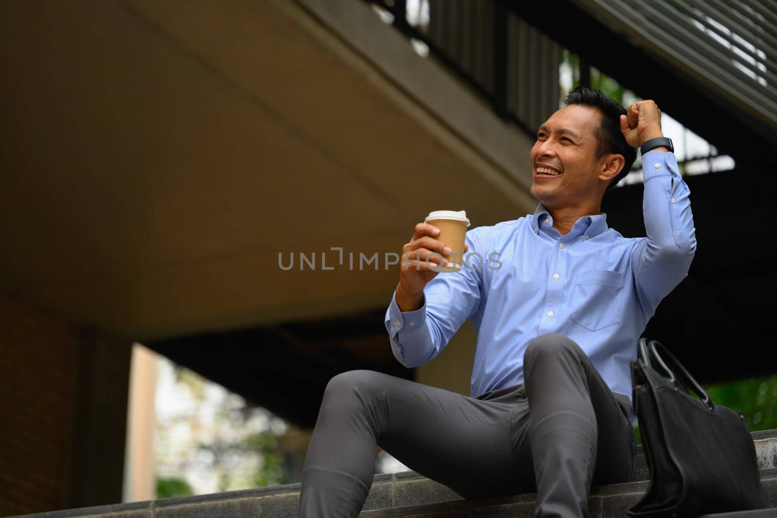 Confident young businessman on the stairs near office building celebrating success by prathanchorruangsak