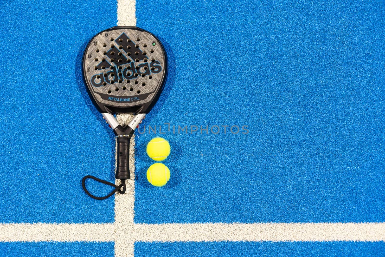 Kyiv, Ukraine, April 18, 2024. Black professional paddle tennis racket and ball with natural lighting on blue background. Horizontal sport theme poster, greeting cards, headers, website and app. High quality photo