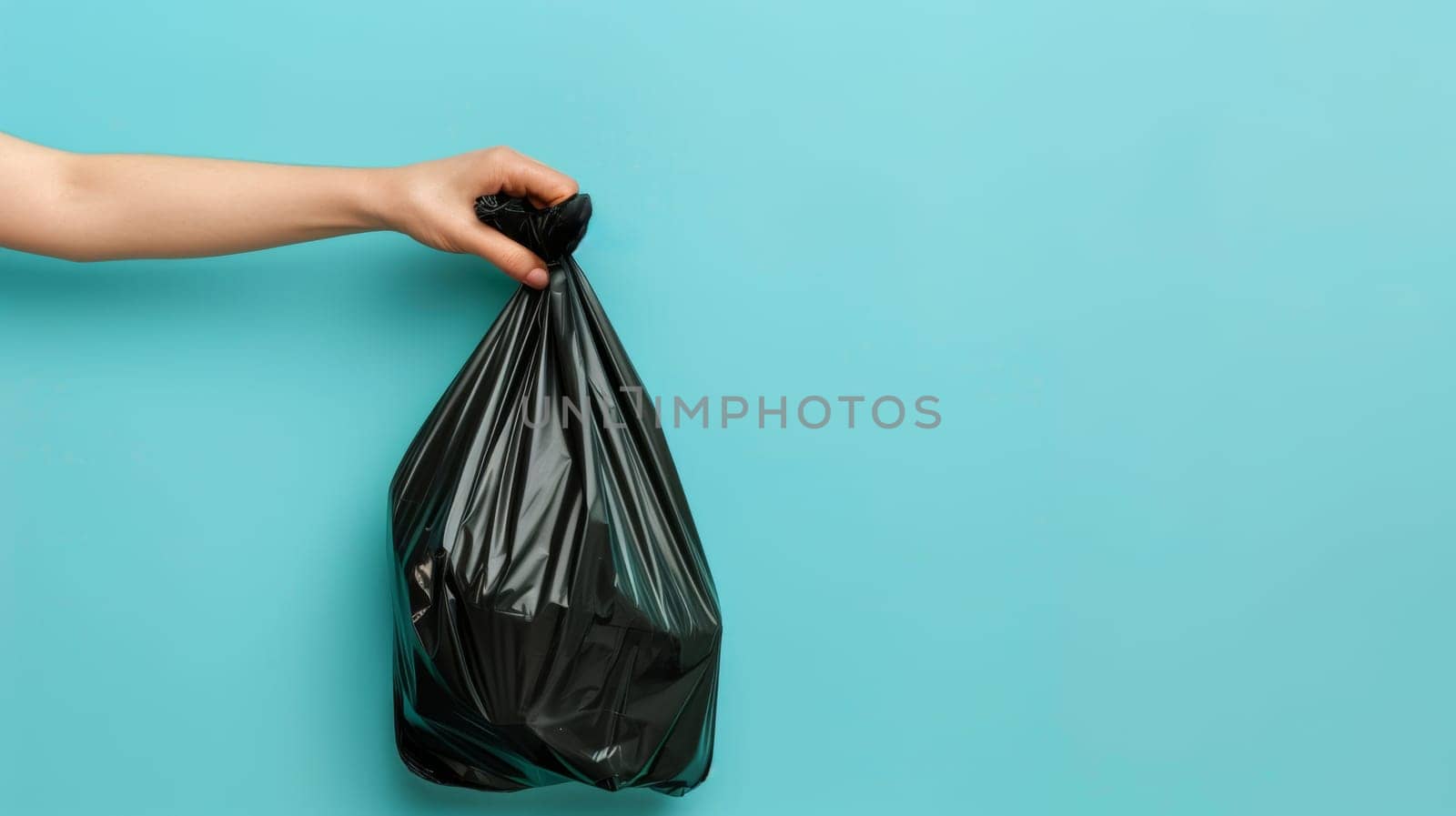 Hand holding a black garbage bag on a blue background.