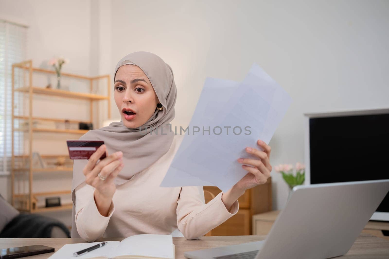 A young Muslim woman is shocked by an excessive bill from an online purchase made with a credit card through an online banking application..