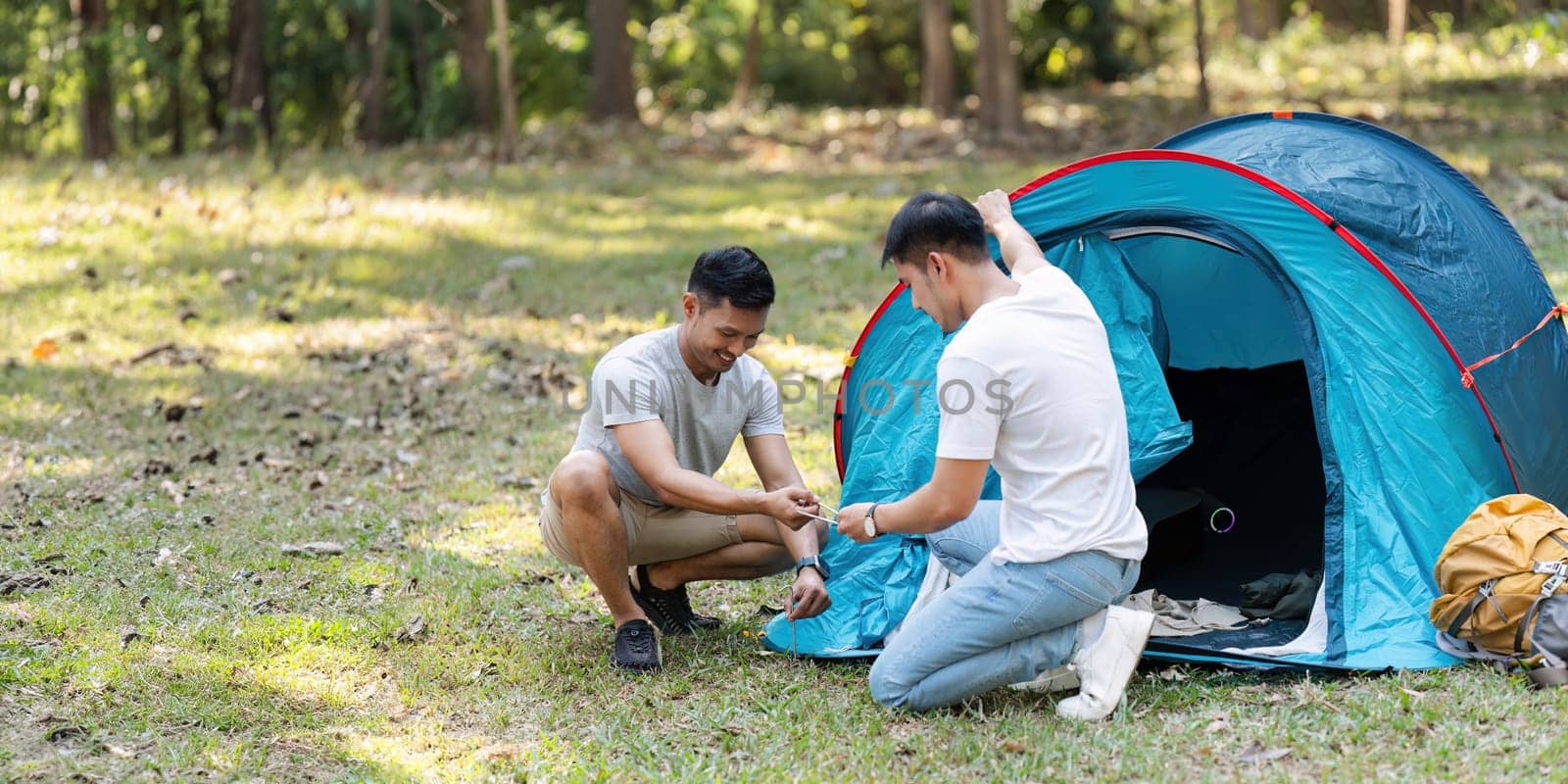 LGBTQIA Gay couple camping together in woods for holidays and helping set up a tent together.