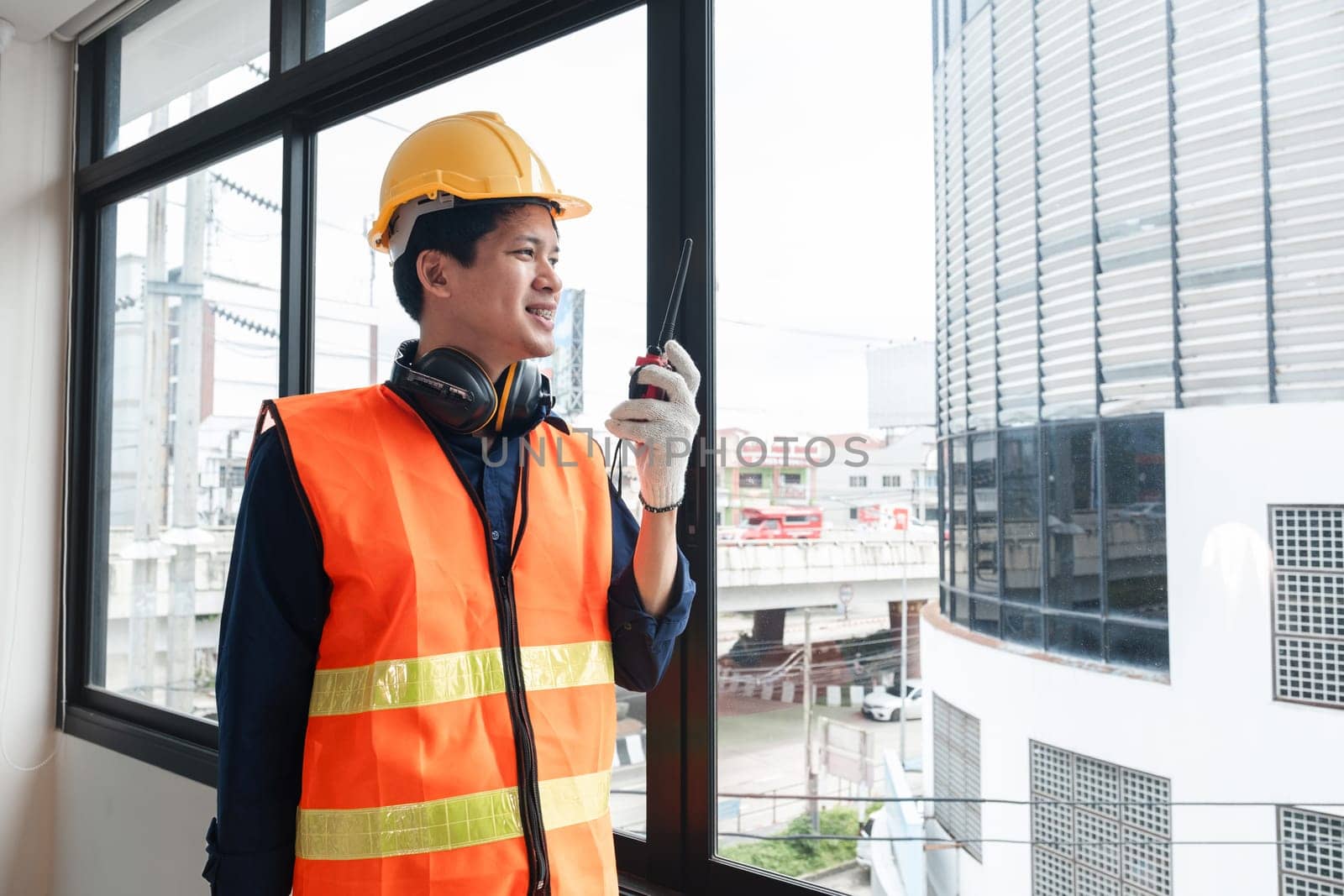 A young engineer stands with a walkie-talkie talking to a team of coordinating engineers at a construction site..