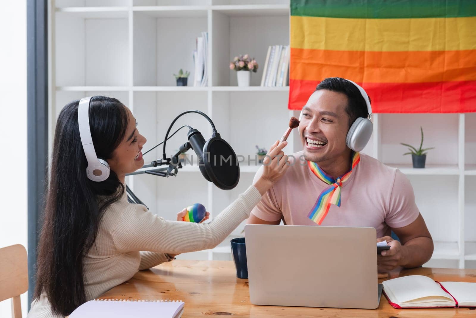 A young gay man and his girlfriend use a laptop and microphone to stream podcast audio at a studio talking about gender liberation. by wichayada