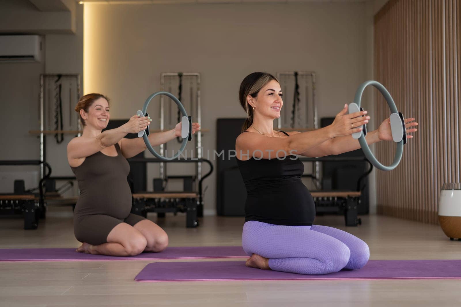 Two pregnant women doing yoga. Exercises with a gymnastic circle for Pilates