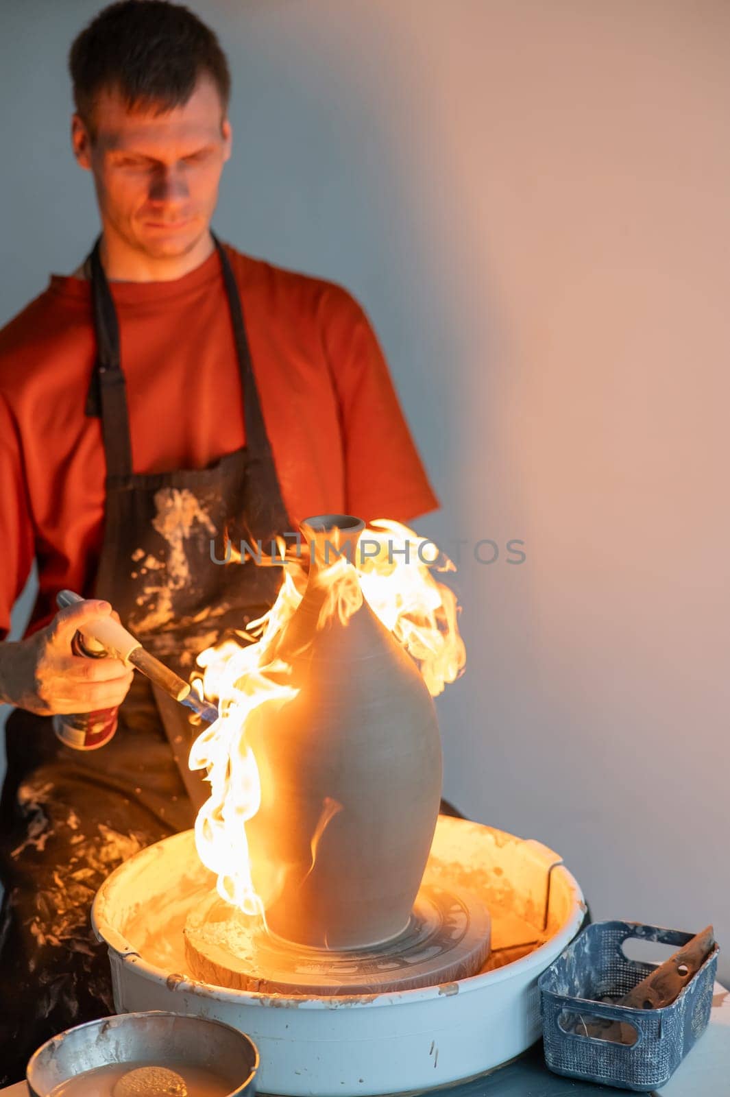 A potter burns a jug with a gas burner on a potter's wheel. Vertical photo