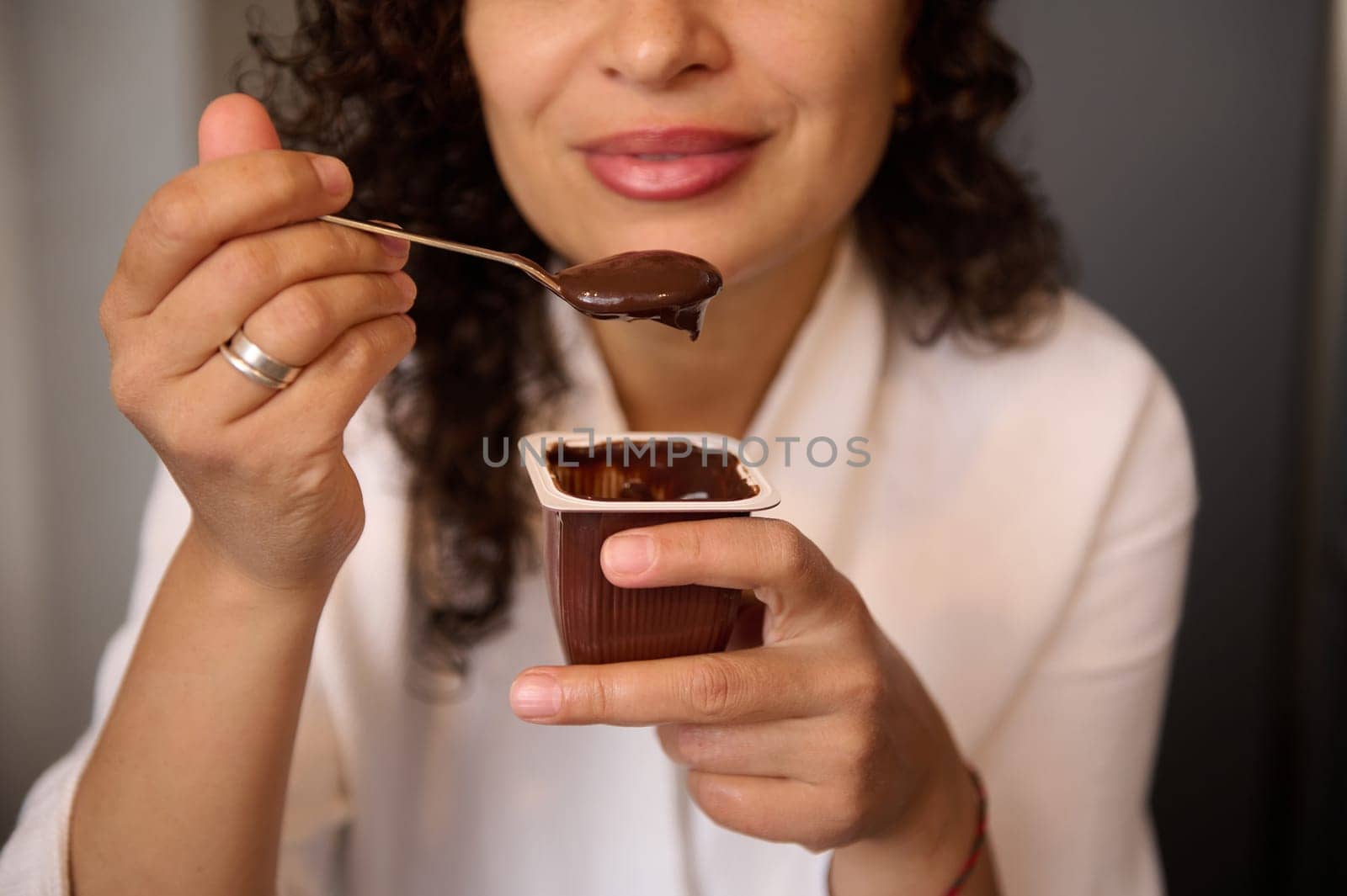 Close-up of a blurred young smiling woman eating delicious chocolate vegan yogurt for breakfast. Healthy eating and diet concept. Food and drink consumerism. by artgf