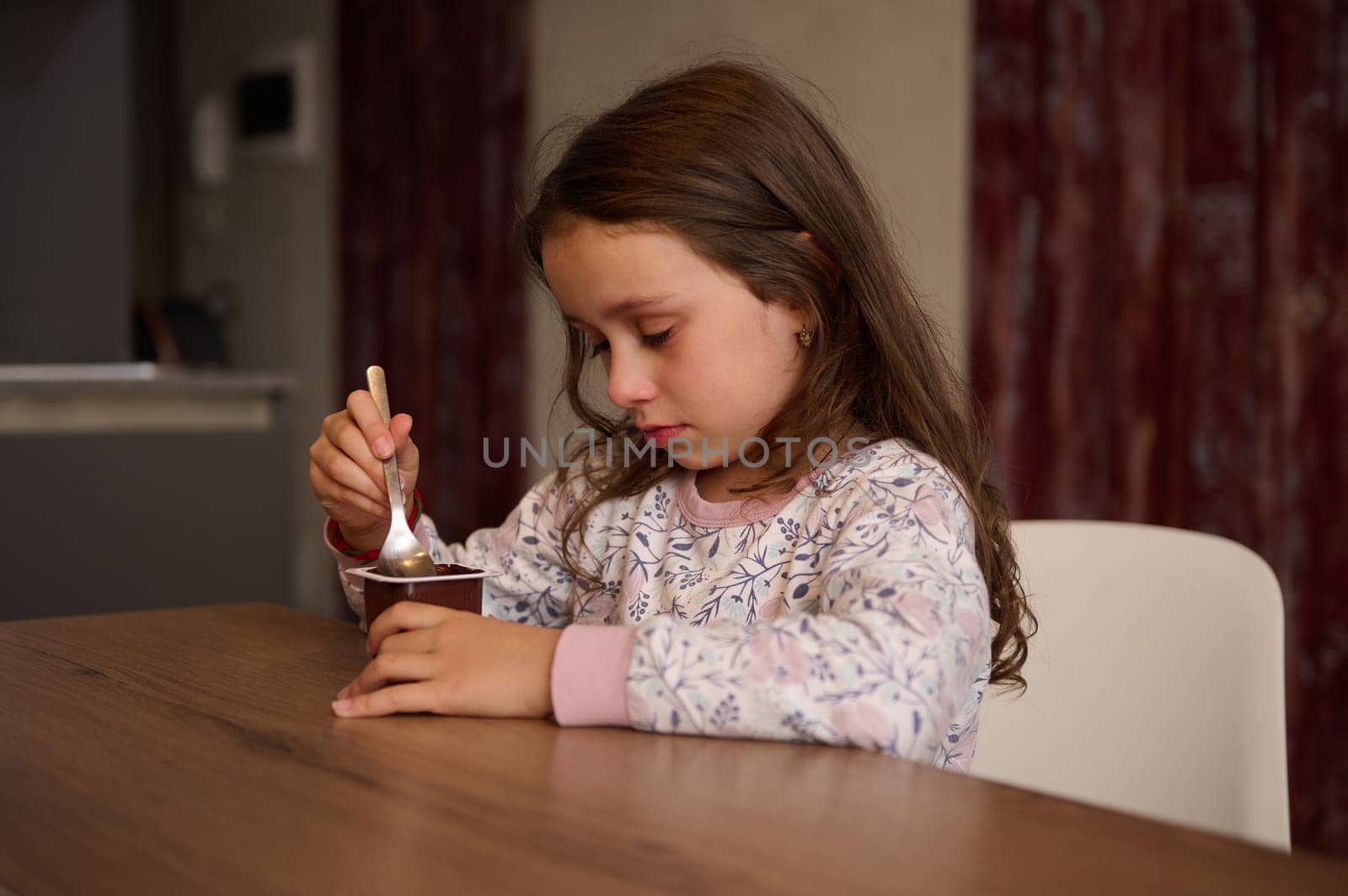 Adorable little child girl eating delicious chocolate vegan yogurt for breakfast. Healthy eating and diet concept. Food and drink consumerism. by artgf