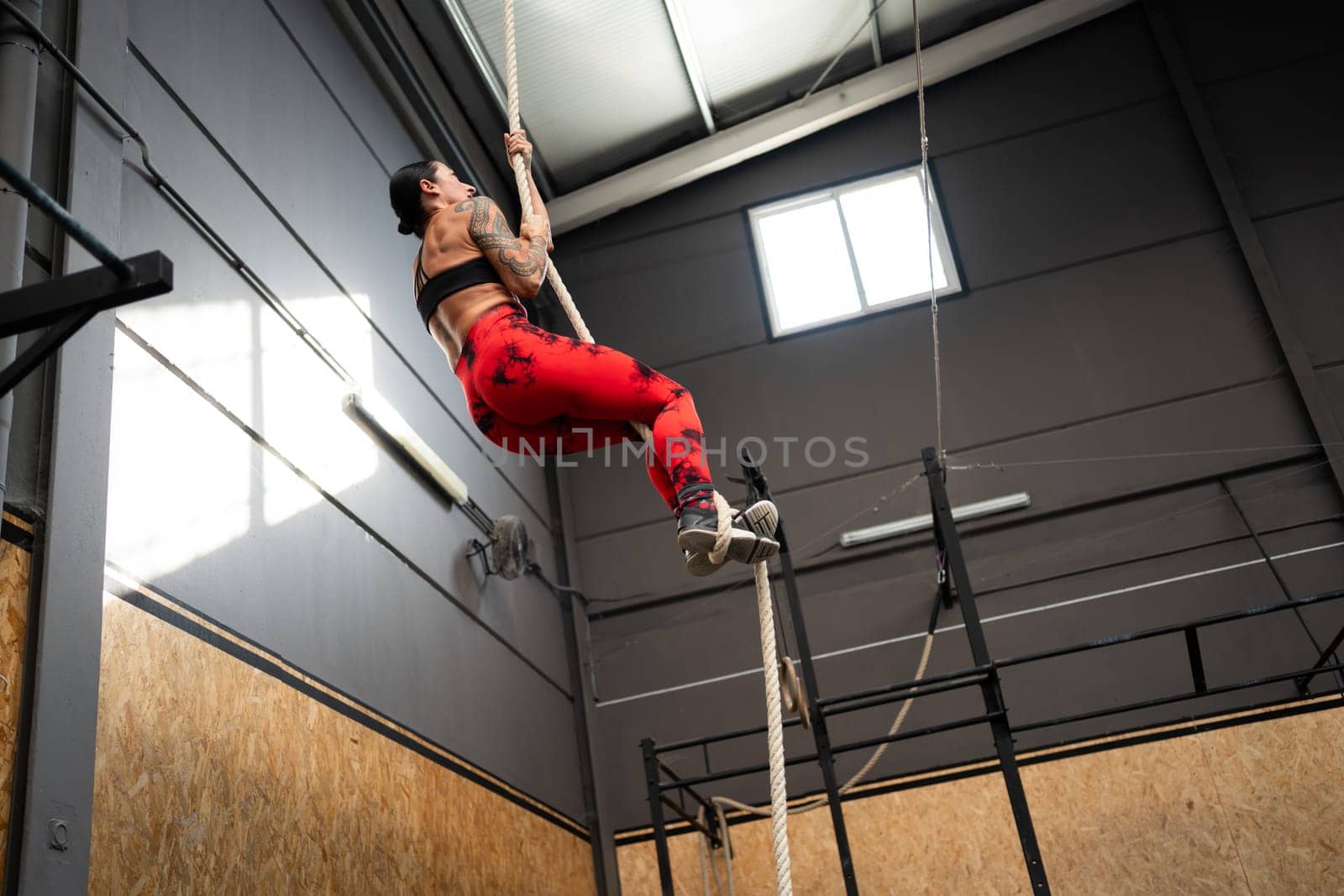 Low angle view photo with copy space of a strong mature woman training climbing a rope in a cross training center