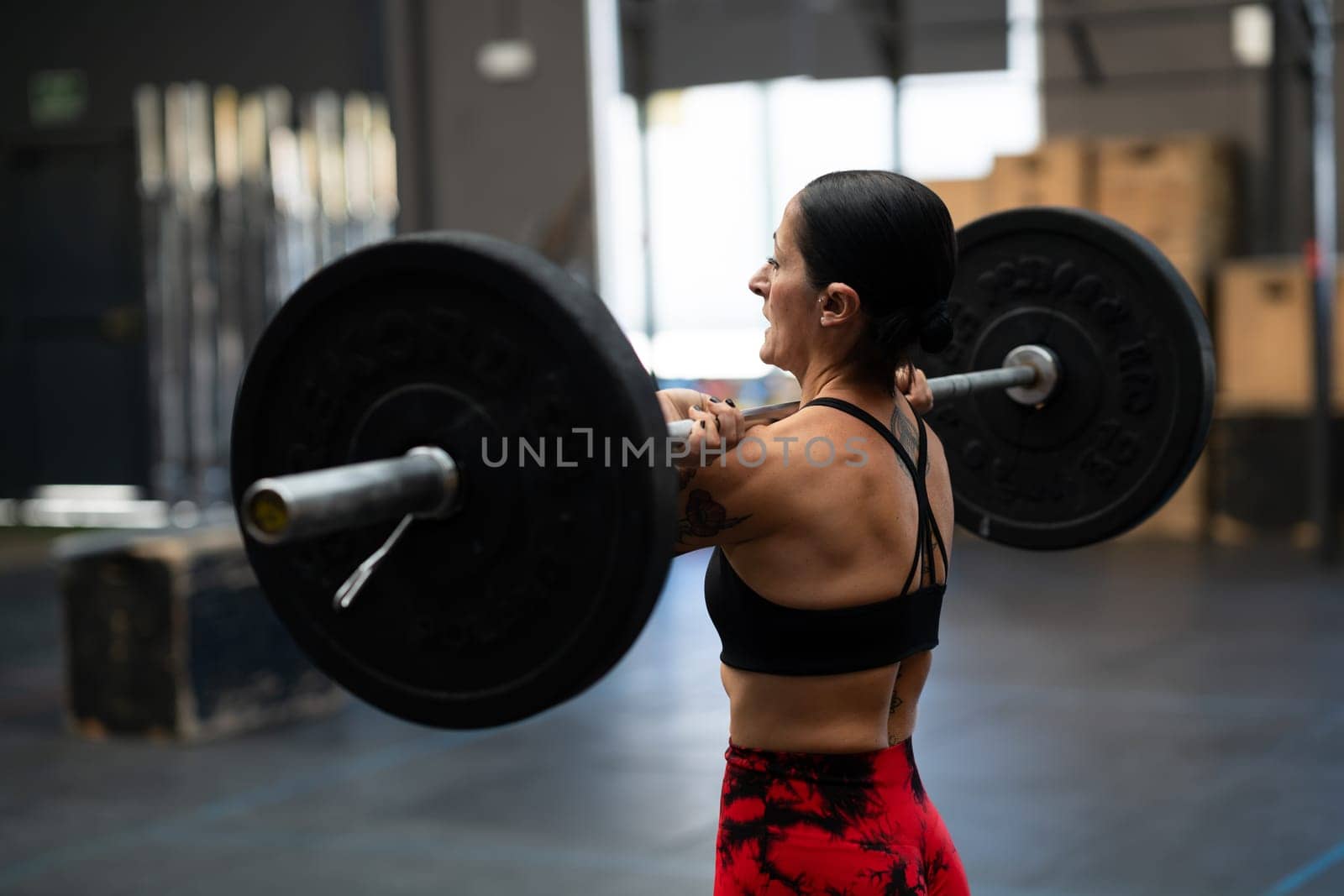 Rear view of a strong mature woman lifting weights in a gym