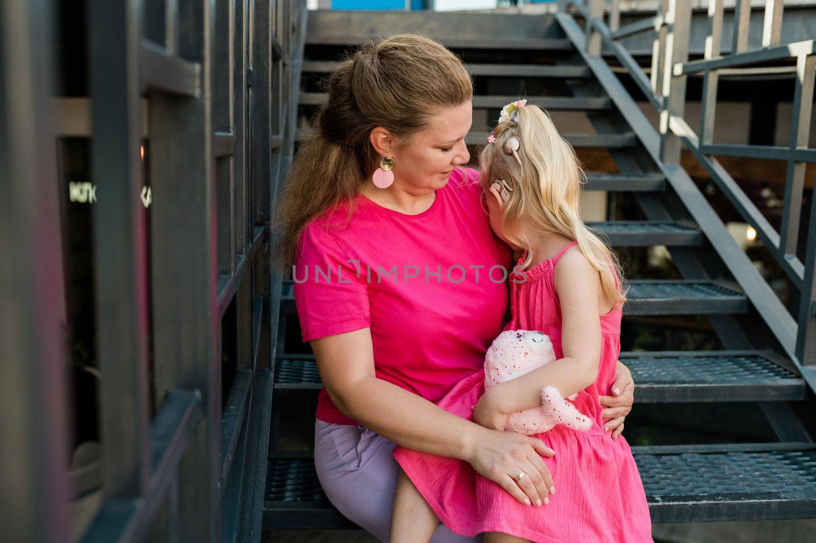 Deaf child with cochlear implant for hearing audio and aid for impairment having fun and laughs with mother outdoor in summer. Sound fitting device to help with communication listening and interaction.