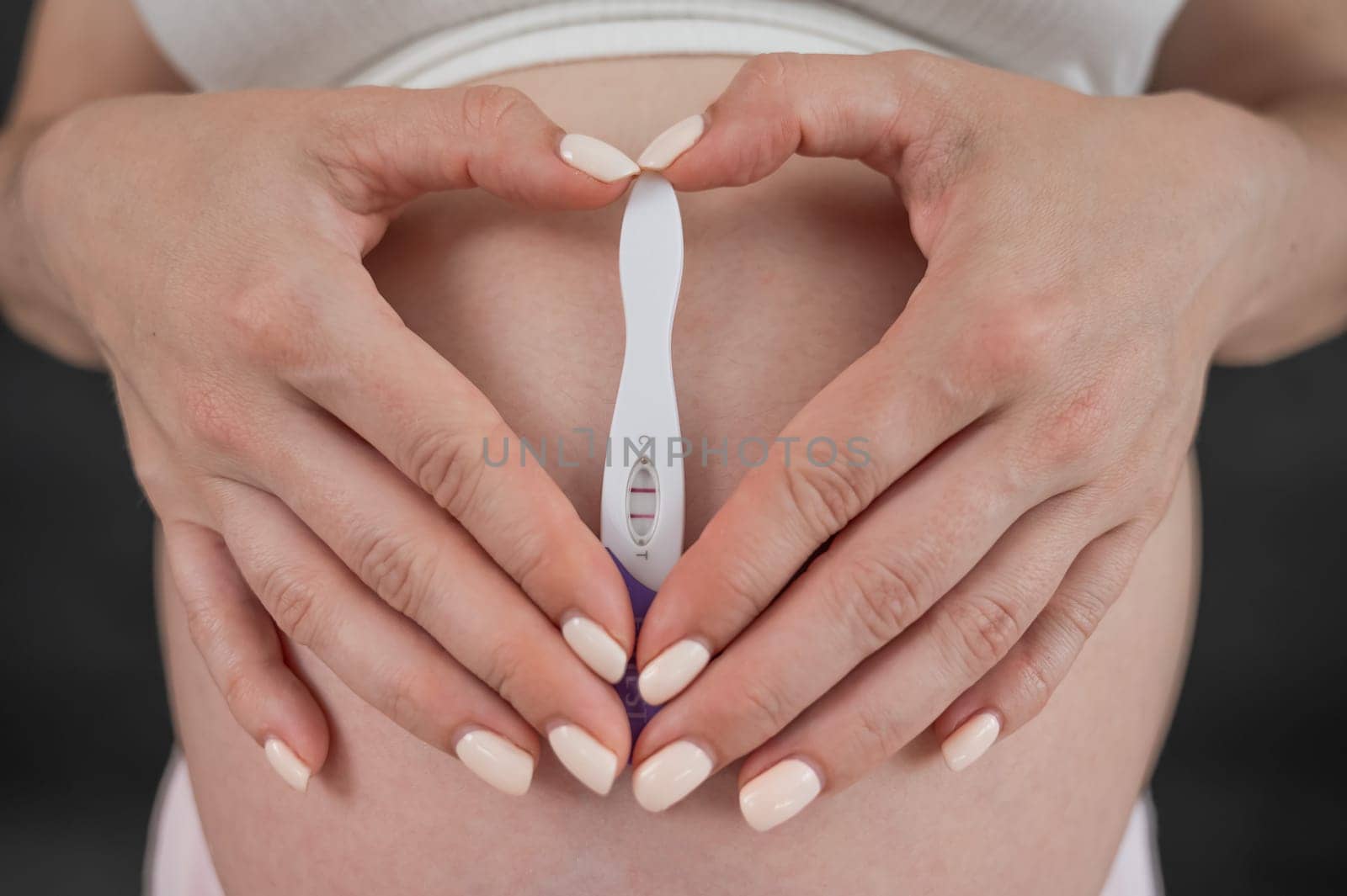 Caucasian woman holding a positive express pregnancy test against the background of her tummy