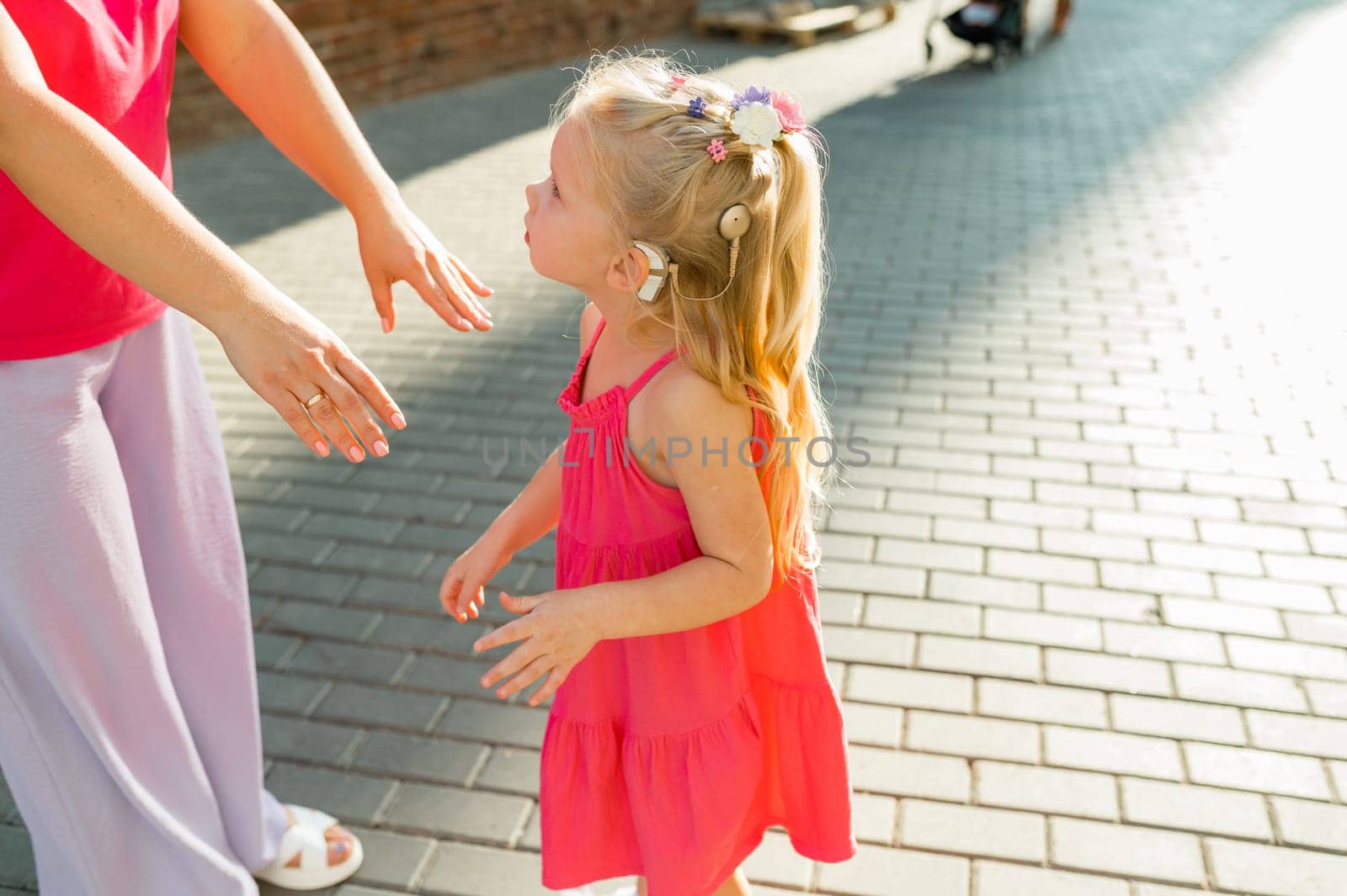 Deaf child with cochlear implant for hearing audio and aid for impairment having fun and laughs with mother outdoor in summer. Sound fitting device to help with communication listening and interaction.