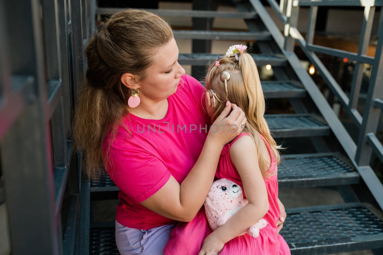 Child girl with cochlear implant with her mother spend time outdoor. Hear impairment and deaf community concept. Deaf and health concept. Diversity and inclusion. Copy space.