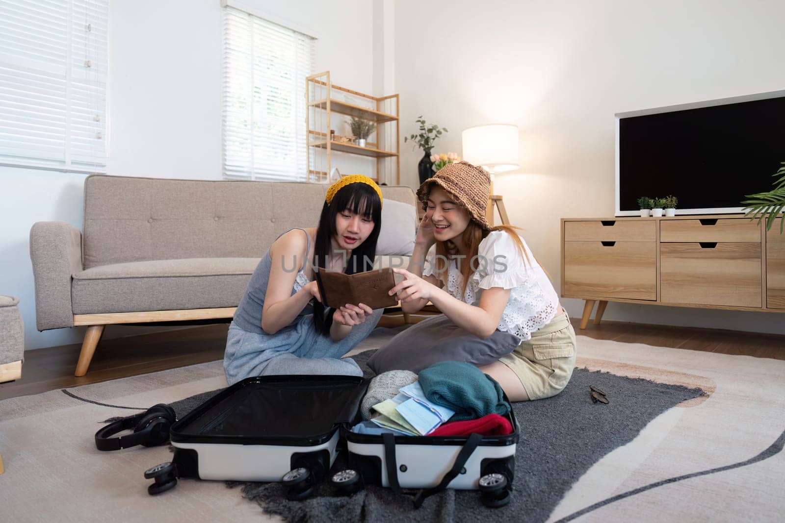 Young Asian woman packing clothes to the suitcase. Preparation for the summertime vacation. Two women are planning a trip and helping to prepare luggage to travel by nateemee