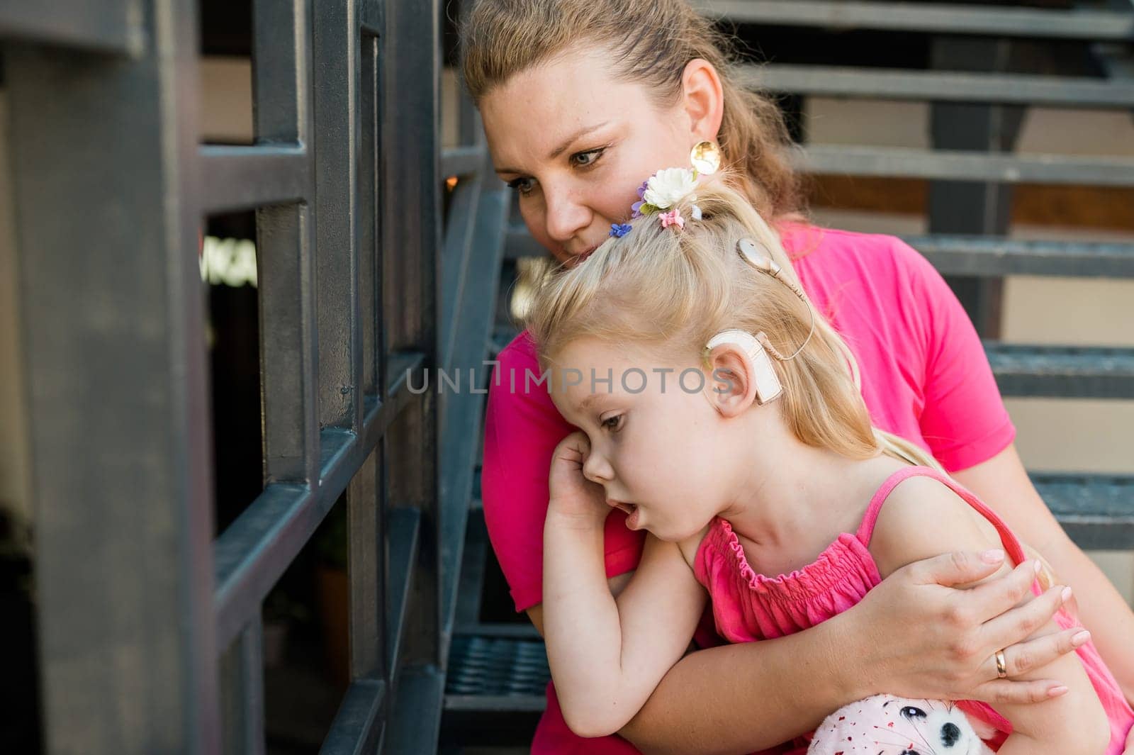 Deaf child with cochlear implant for hearing audio and aid for impairment having fun and laughs with mother outdoor in summer. Sound fitting device to help with communication listening and interaction.