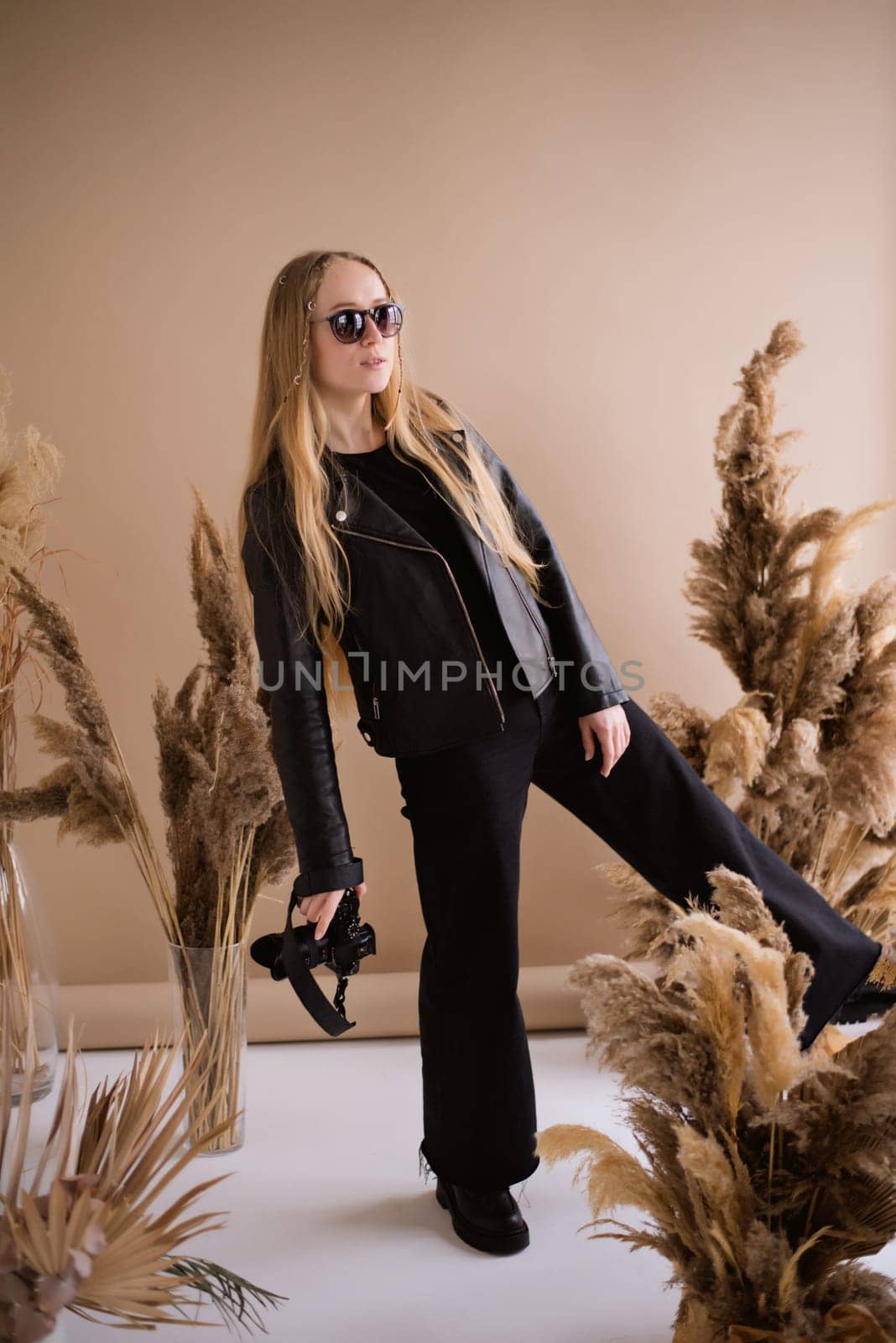 A crazy woman photographer, a blonde with a camera, happy and smiling in the production studio. Wearing a black clothes on a brown background