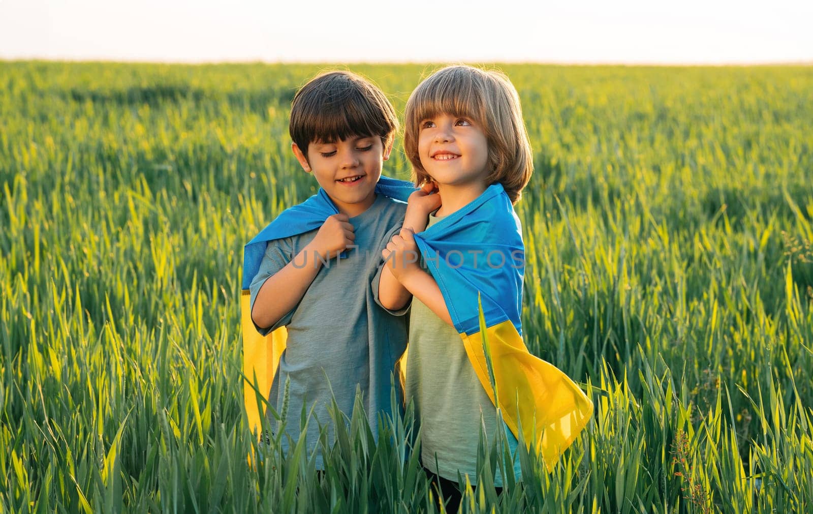 Happy glad boys - Ukrainian patriots children with national flag on in fresh green field. Ukraine, family, brothers twins, best friends, peace, freedom, win in war.