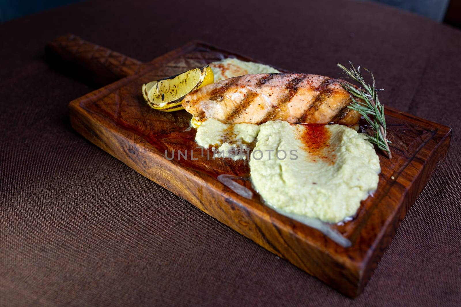 A mouthwatering grilled salmon fillet topped with a zesty lemon-herb butter sauce, presented elegantly on a rustic wooden serving board.