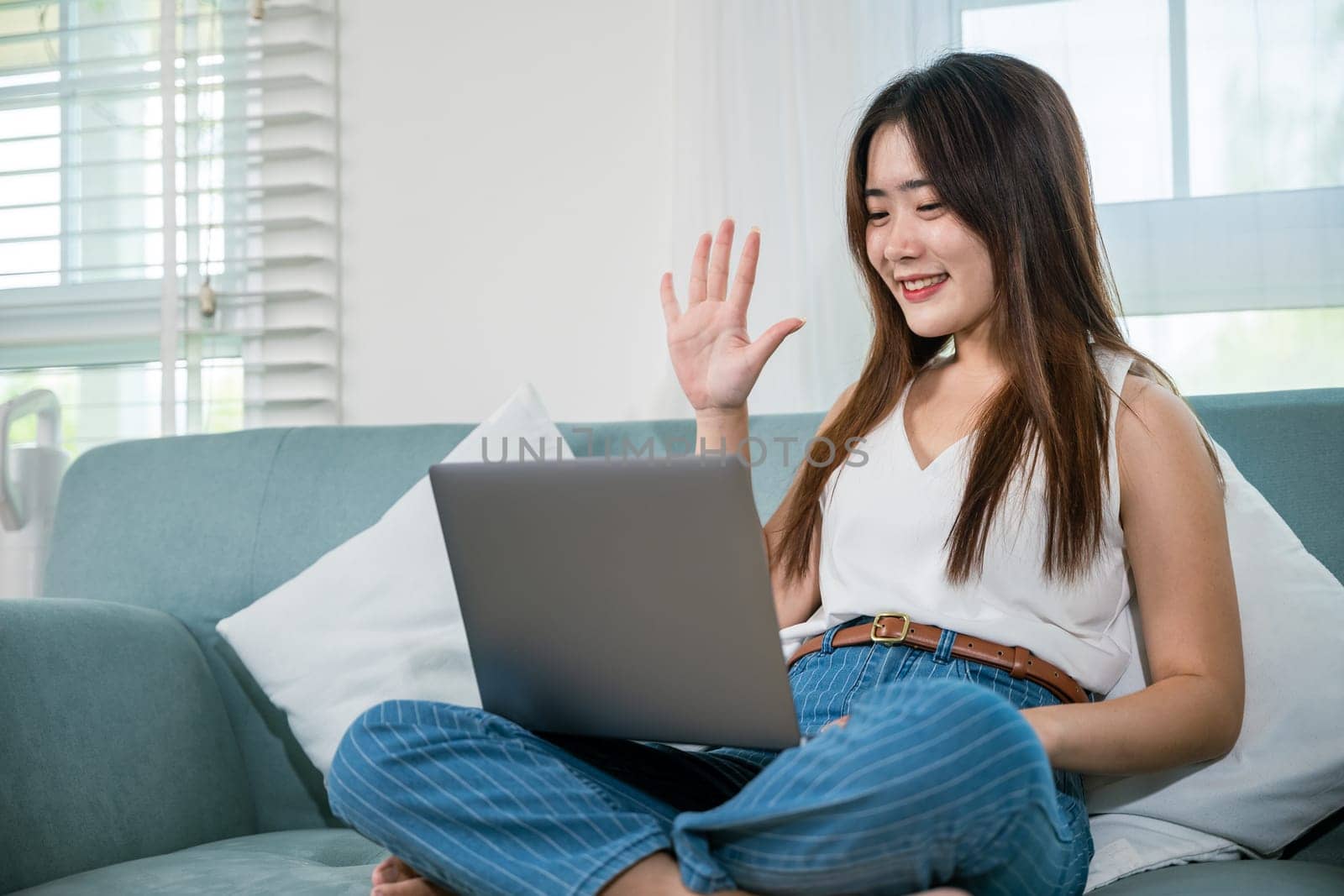 Happy woman typing email on notebook computer, Asian young female smiling sitting relaxing on sofa using laptop in living room at home, freelance browsing through the internet during free time