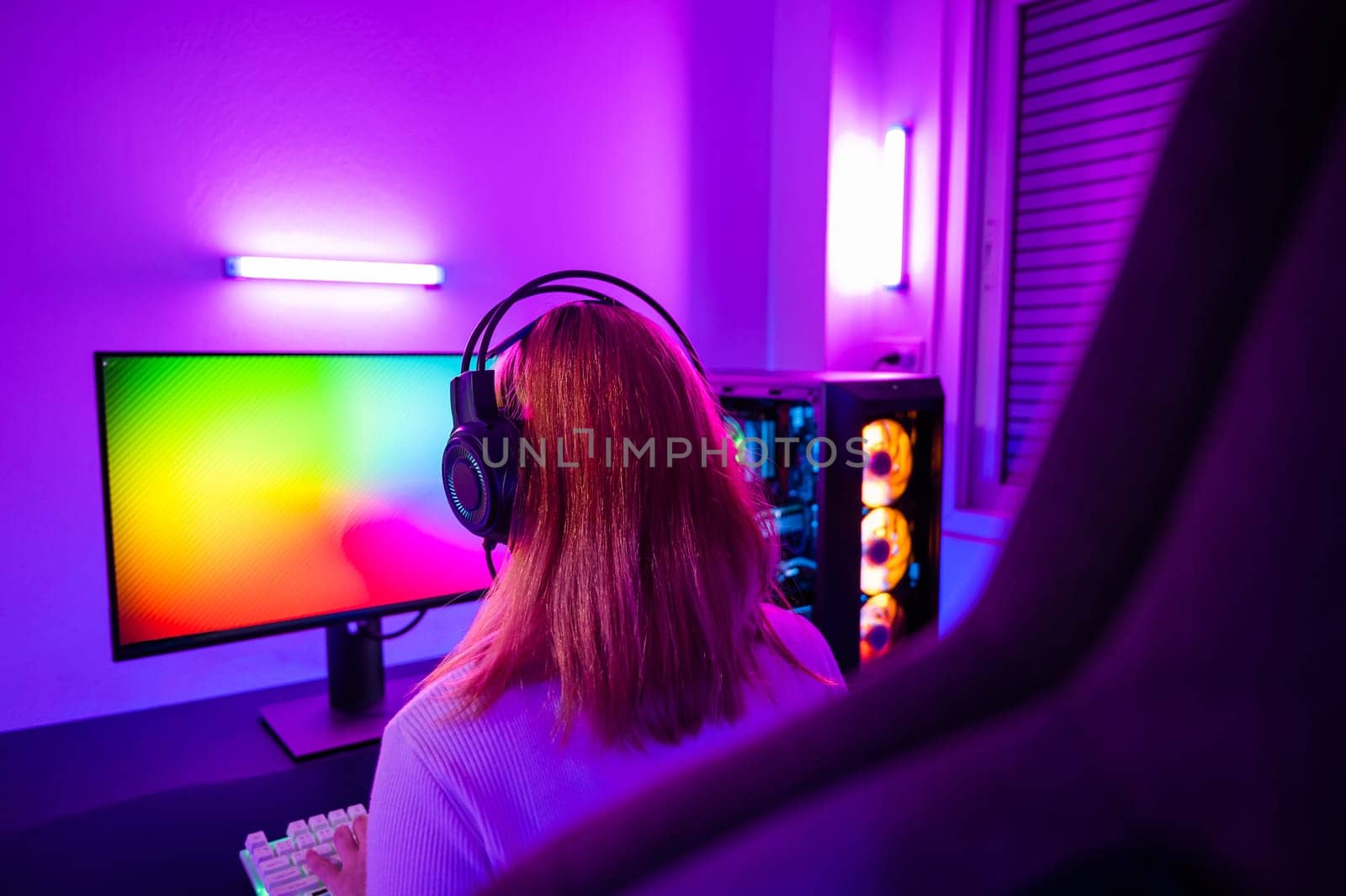 Asian woman gamer wearing gaming headphones holding joystick console to play video game and streaming online on computer PC neon light at home, tournament player E-Sport concept