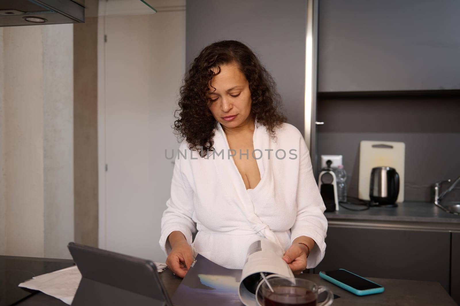 Multi ethnic young pretty woman analyzing the expenses and costs for paying bills, standing at desk at home with documents in hands. Finance and home management concept, planning budget.