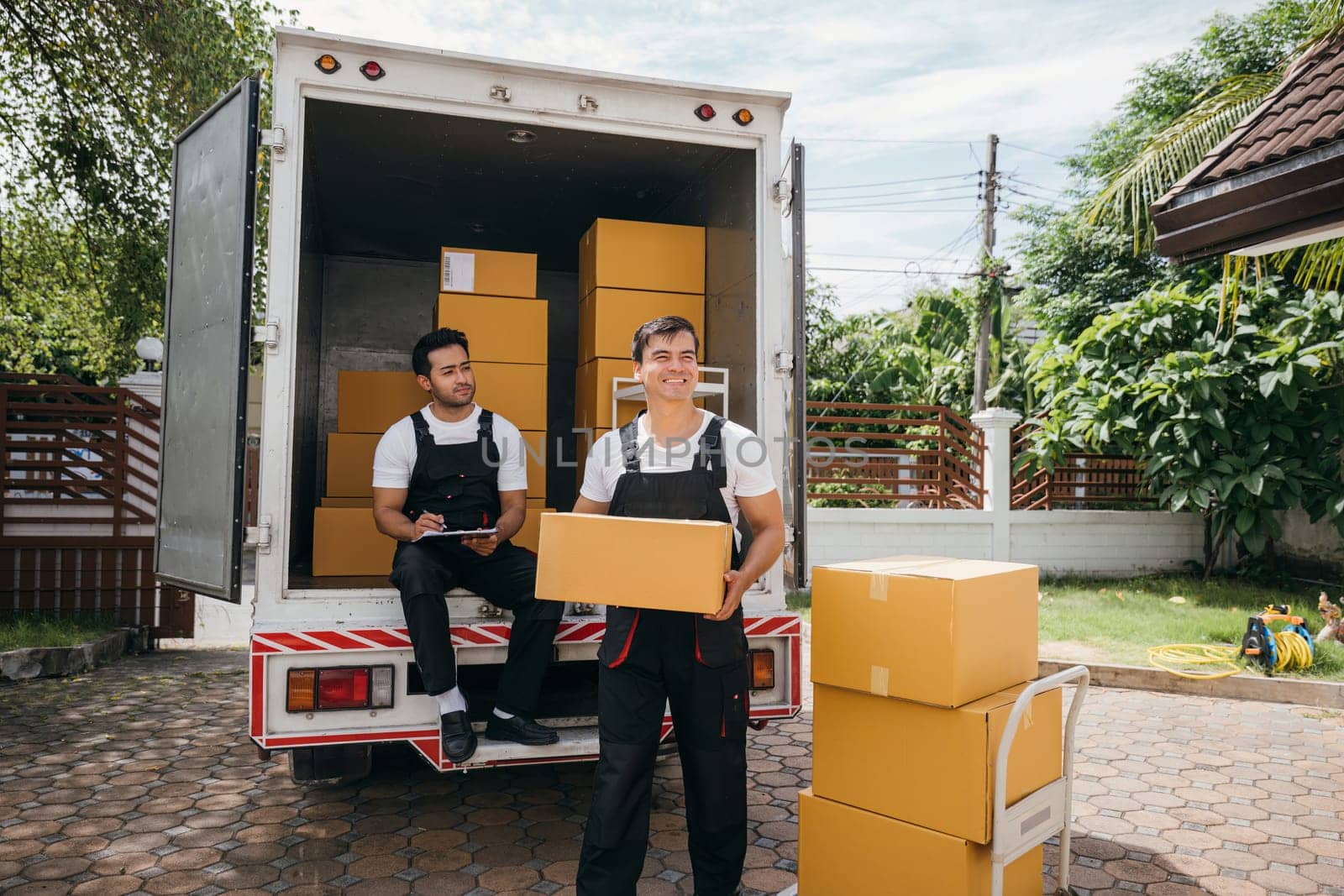 Delivery men unload boxes from a truck. Movers in uniform cooperate in a relocation service. Teamwork and cooperation among colleagues. Smiling workers carrying boxes. relocation teamwork Moving Day by Sorapop