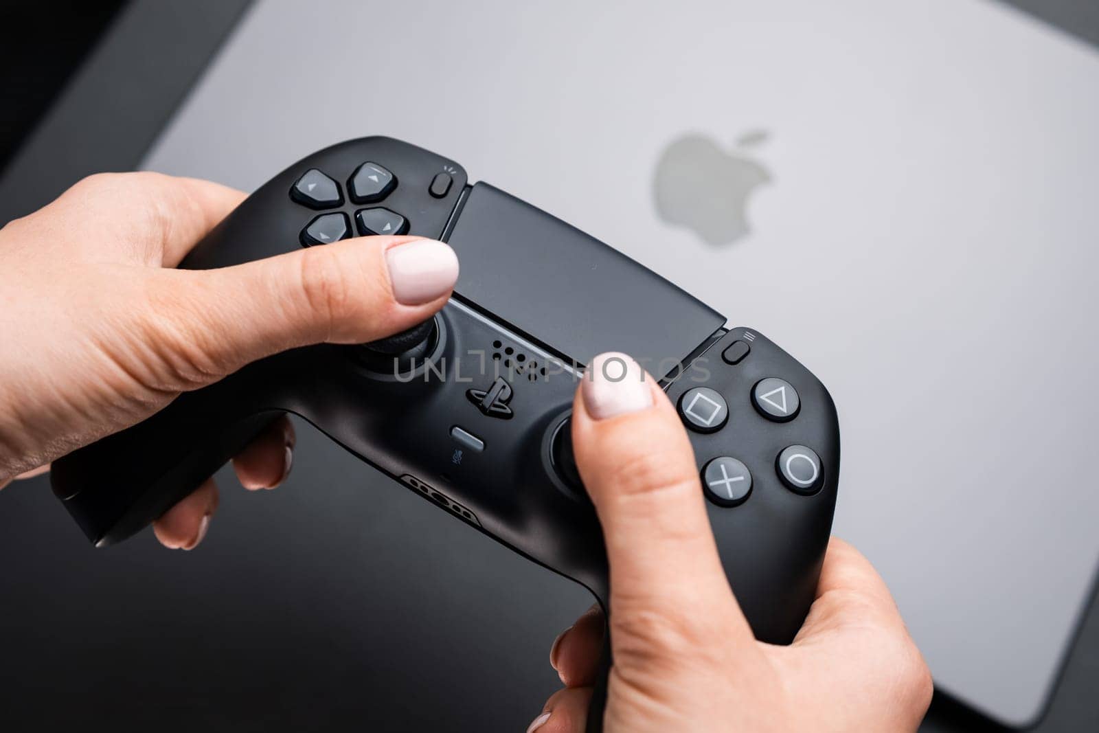 BERLIN , GERMANY - FEBRUARY 14 2024: Video game controller in womans hand against Macbook pro.