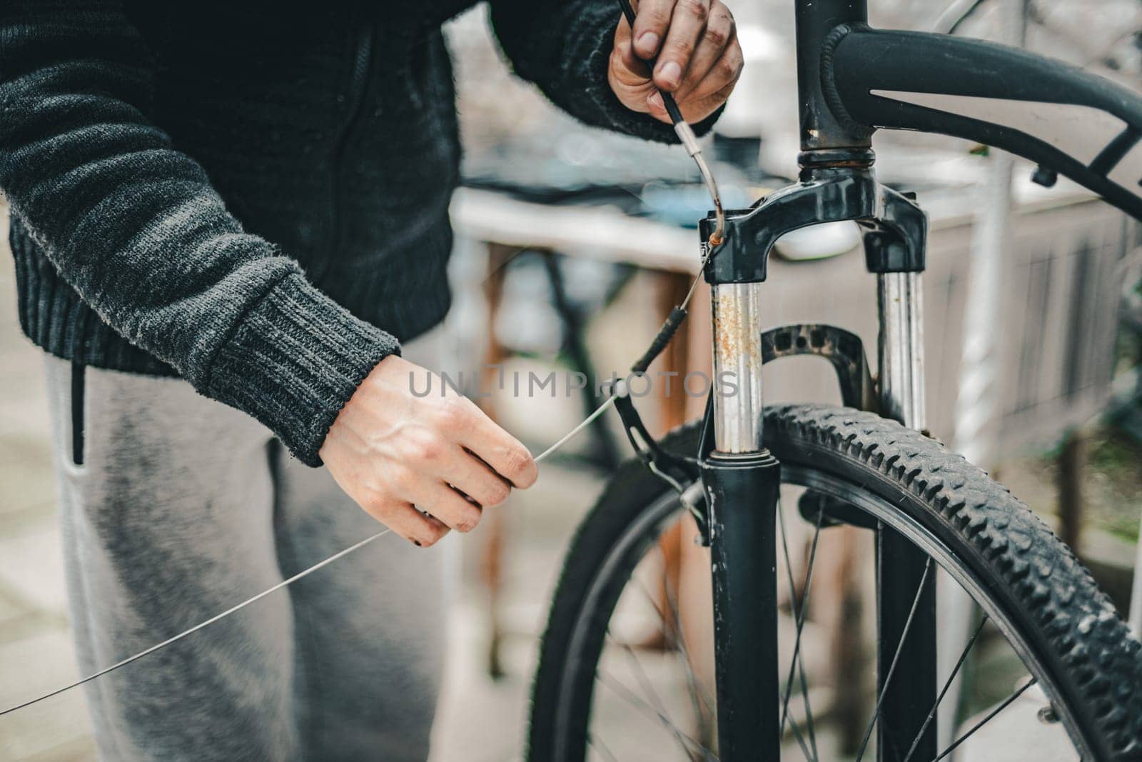 A young man pulls a brake cable on the handlebars of a bicycle. by Nataliya