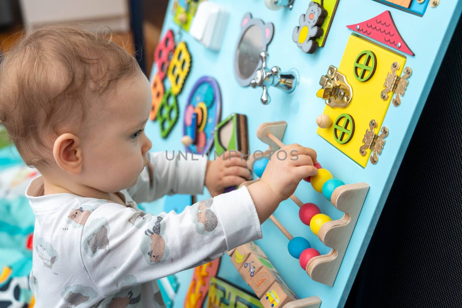 Profile of a cute baby playing with wooden elements on a busy board.