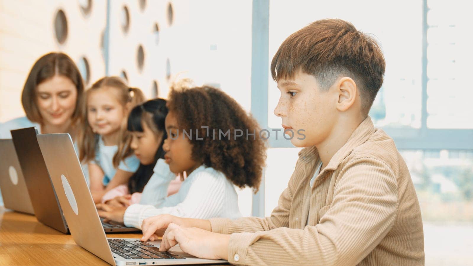 Boy playing laptop with multicultural friend learning prompt at STEM technology class. Multicultural student study about engineering code and programing system with blurring background. Erudition.