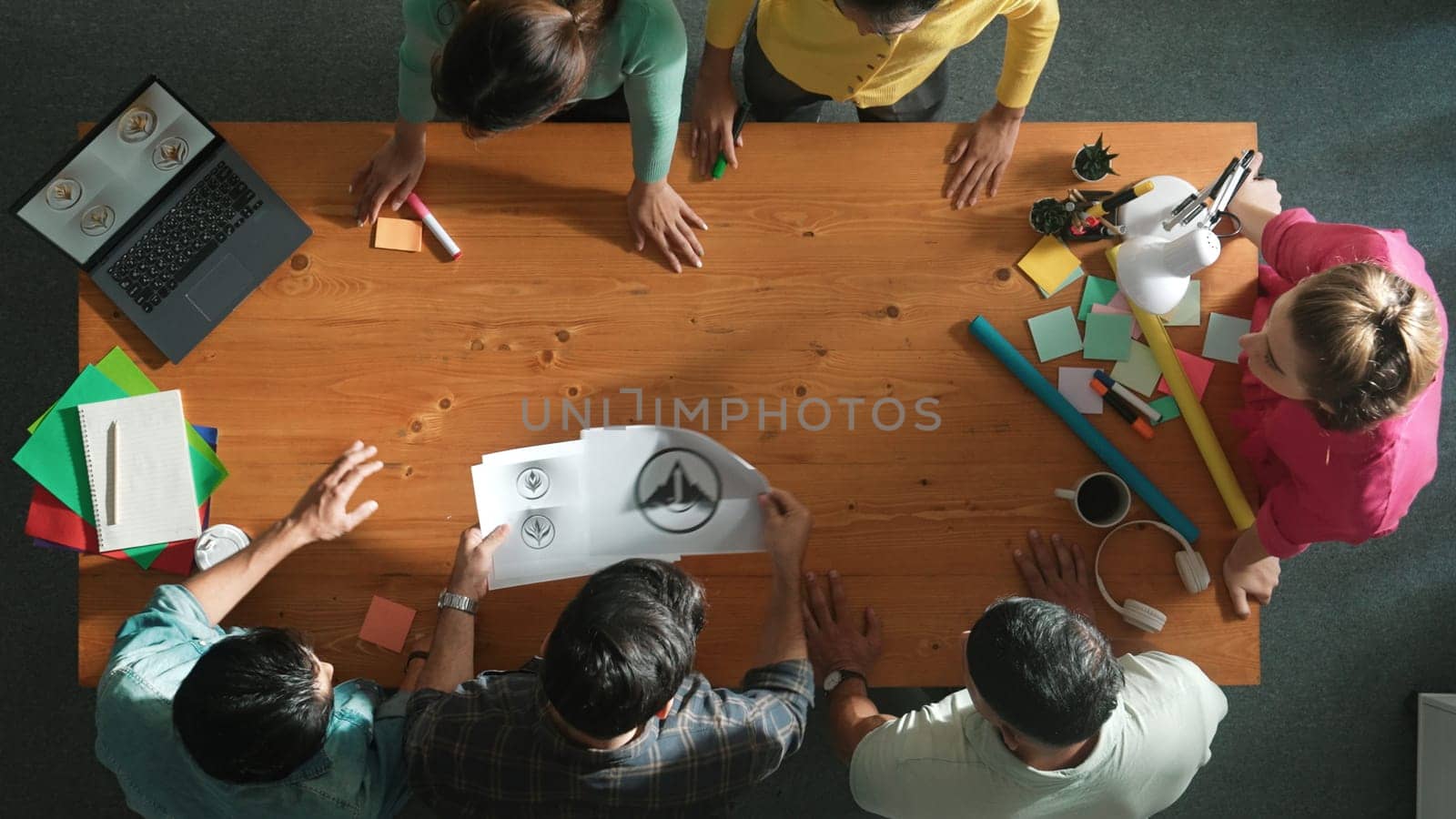 Top view of business team put graphic logo on meeting table with laptop and paper and start to design while explain idea. Manager explaining concept art while placed logo on meeting table. Symposium.