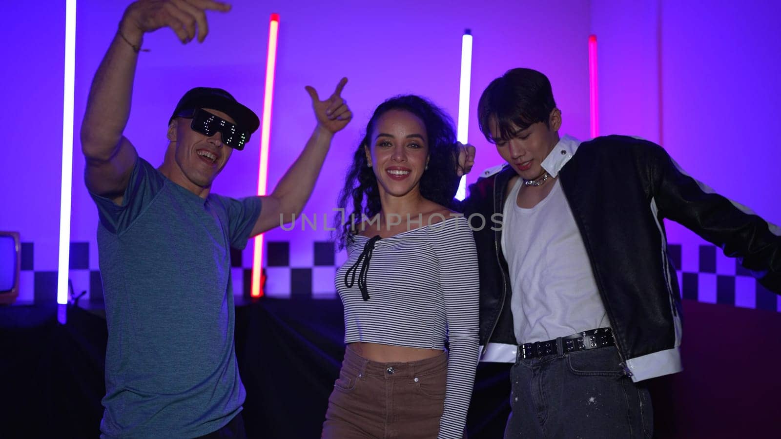 Diverse street dancer moving to city pop music at party with neon light while man wearing fancy glasses. Attractive hipster perform or practicing dancing together while looking at camera. Regalement.