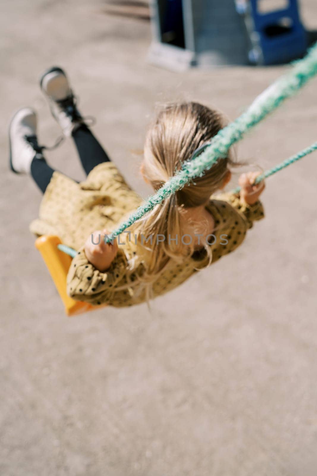 Little girl swings on a rope swing on the playground and looks away. Top view. High quality photo