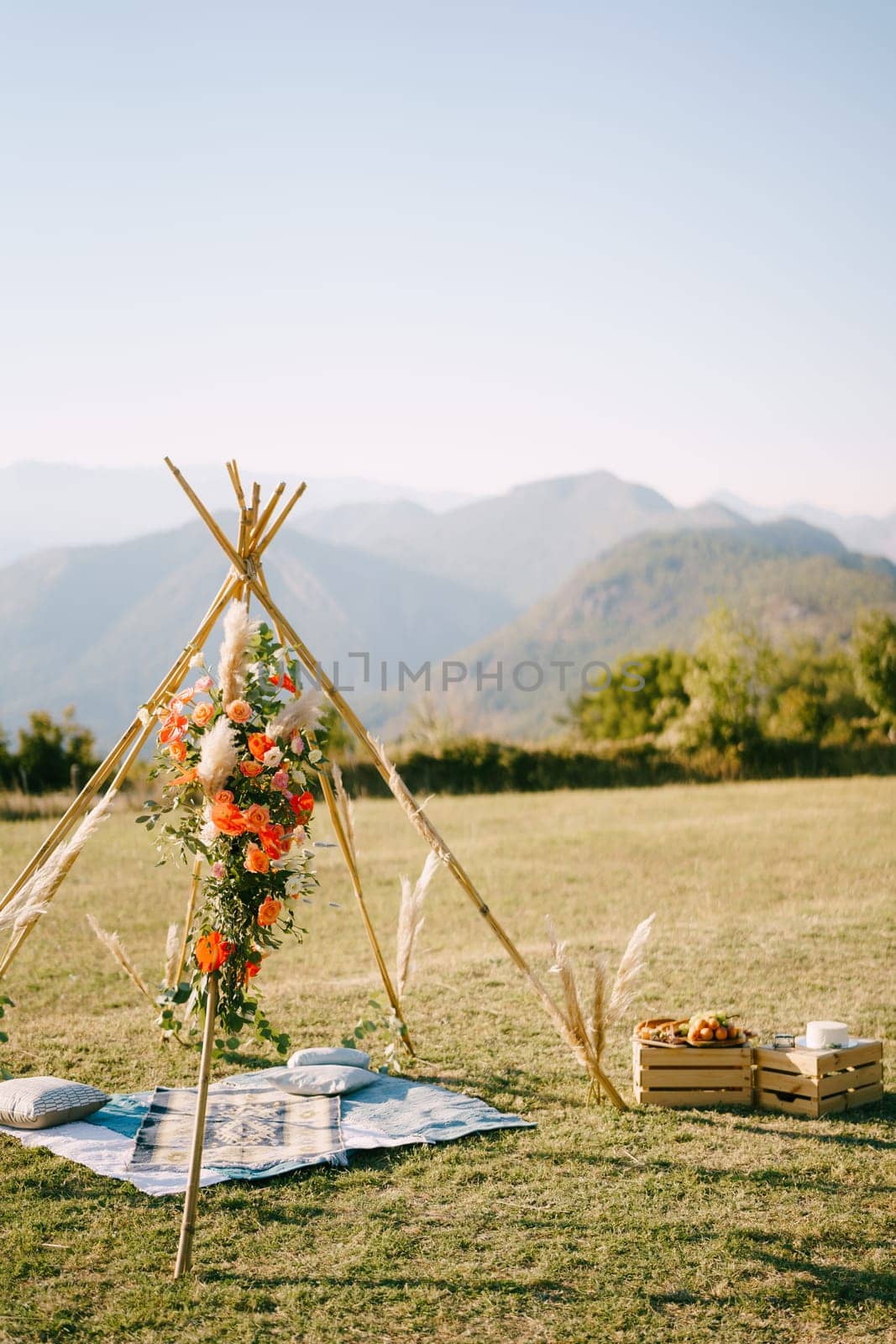 Wedding wigwam arch stands on a green meadow next to boxes of food by Nadtochiy