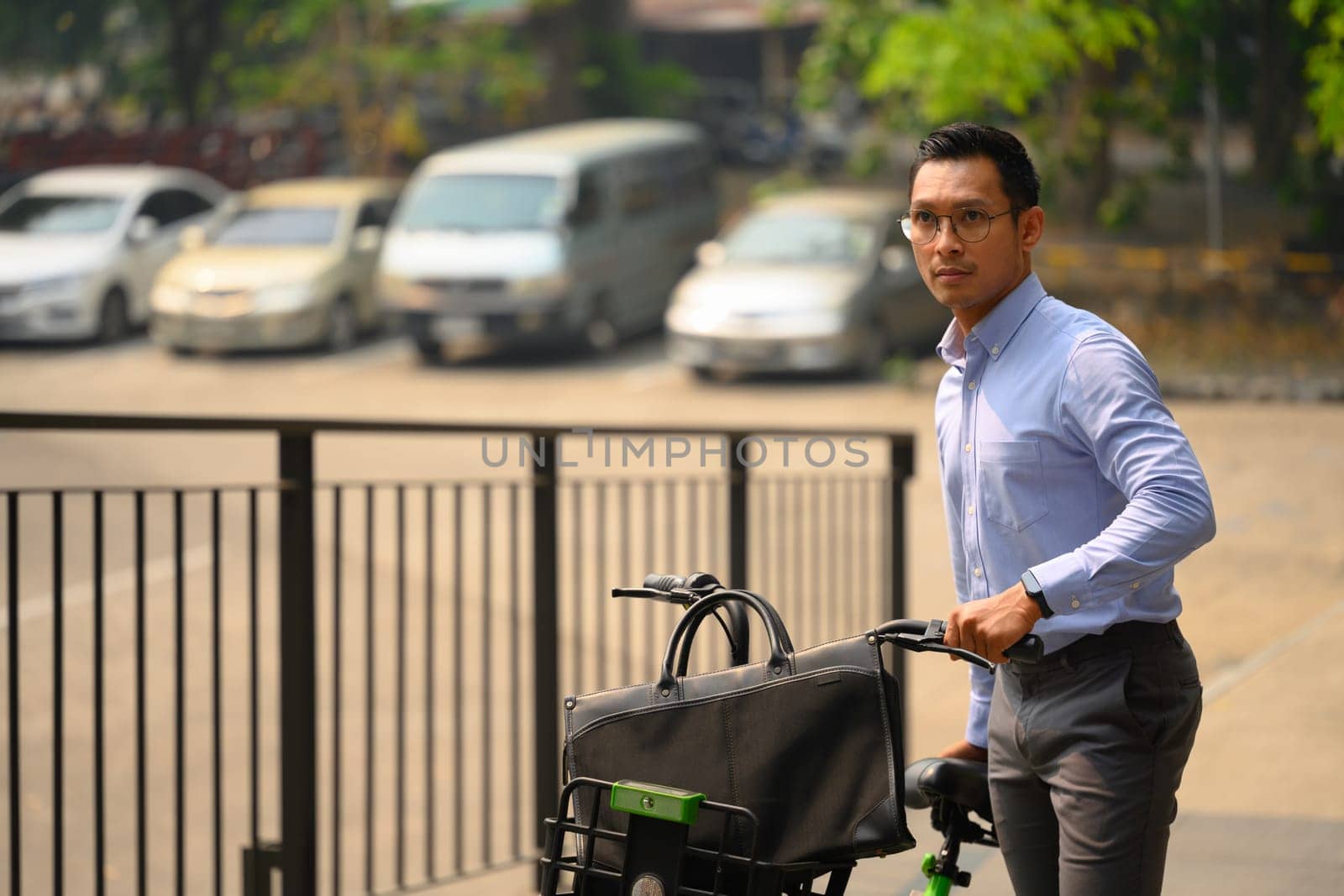 Businessman pushing bicycle while going to work on a sunny morning. Eco transportation.