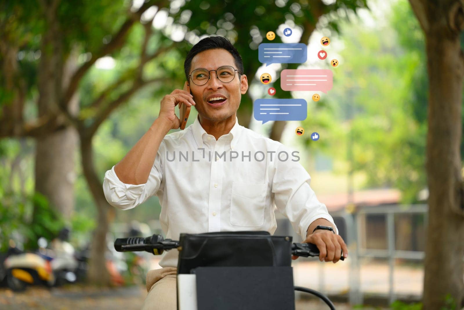Happy male worker having phone call sitting on his bike at city park.