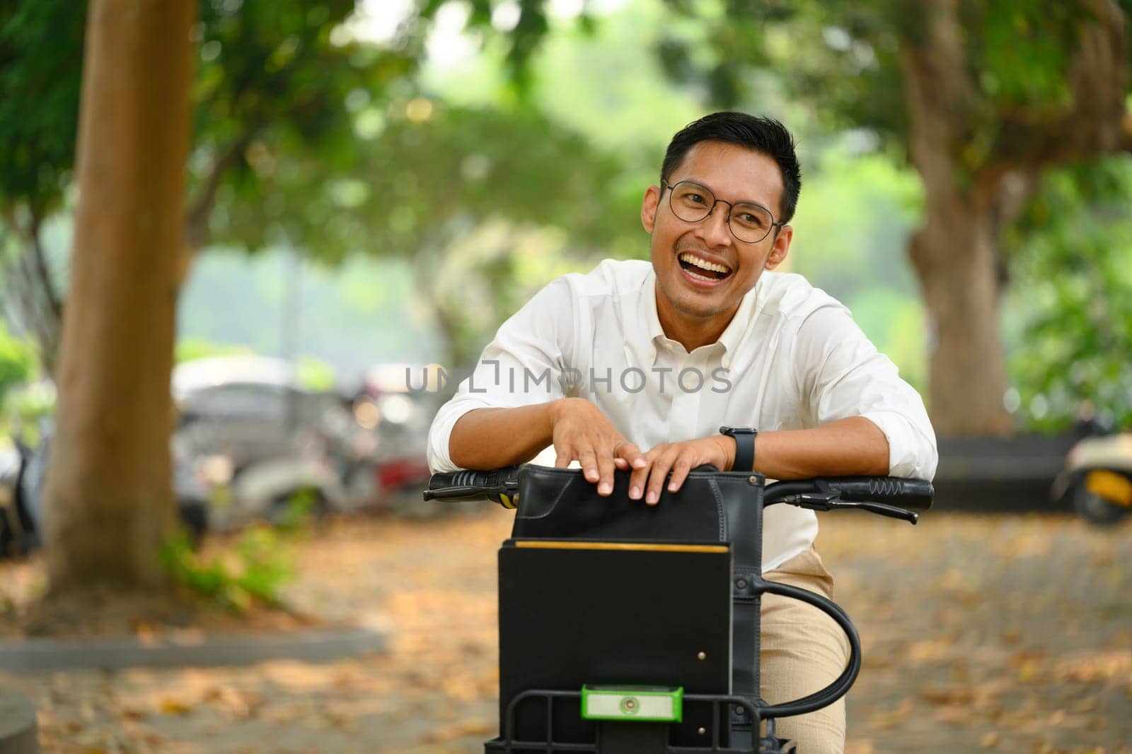 Cheerful Asian male office worker with bicycle in city park. Active lifestyle and transport concept.