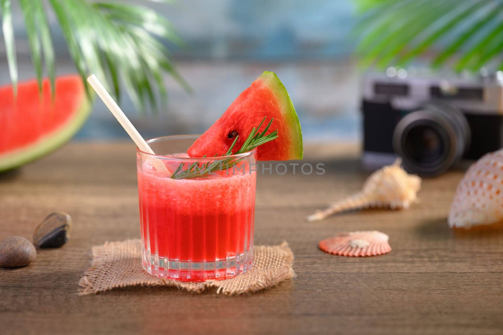 Glass of fresh watermelon juice on wooden table with seashells and camera. Summer drink concept.
